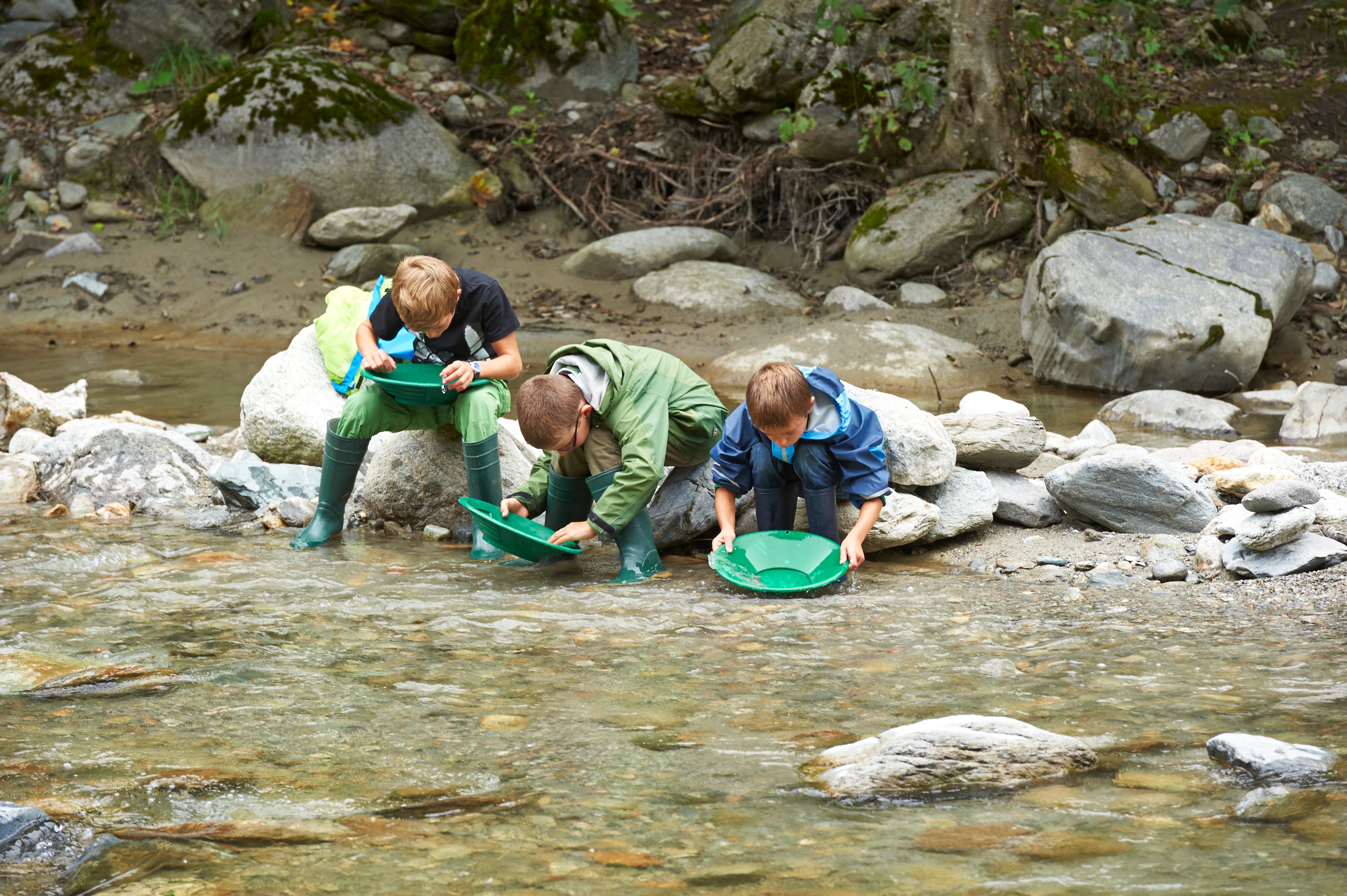 Three boys wash gold in a river.
