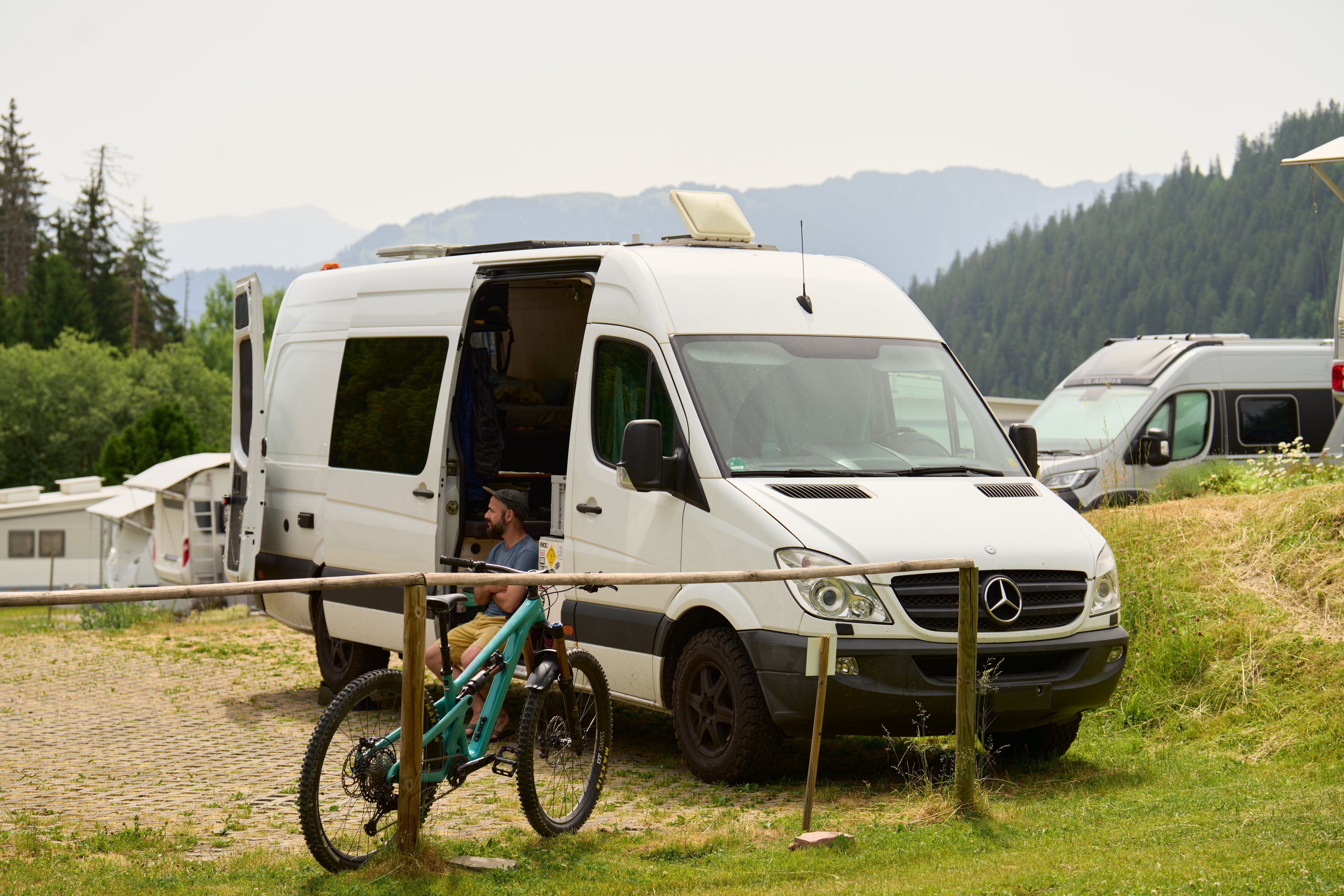 Un uomo è seduto nel suo camper con una mountain bike appoggiata alla recinzione.