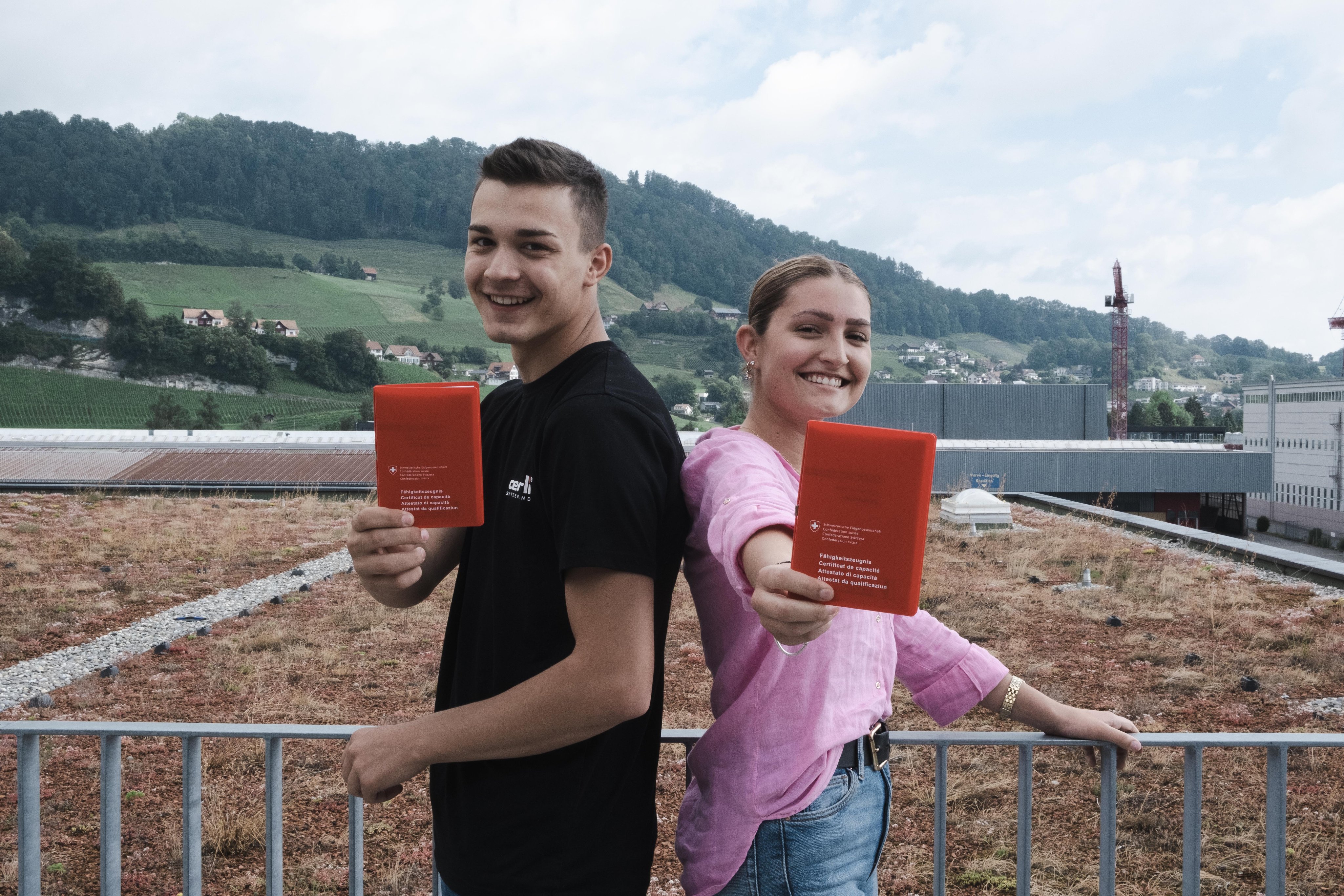 Lehrlinge stehen draussen und halten ein Zertifikat in der Hand und lächeln in die Kamera