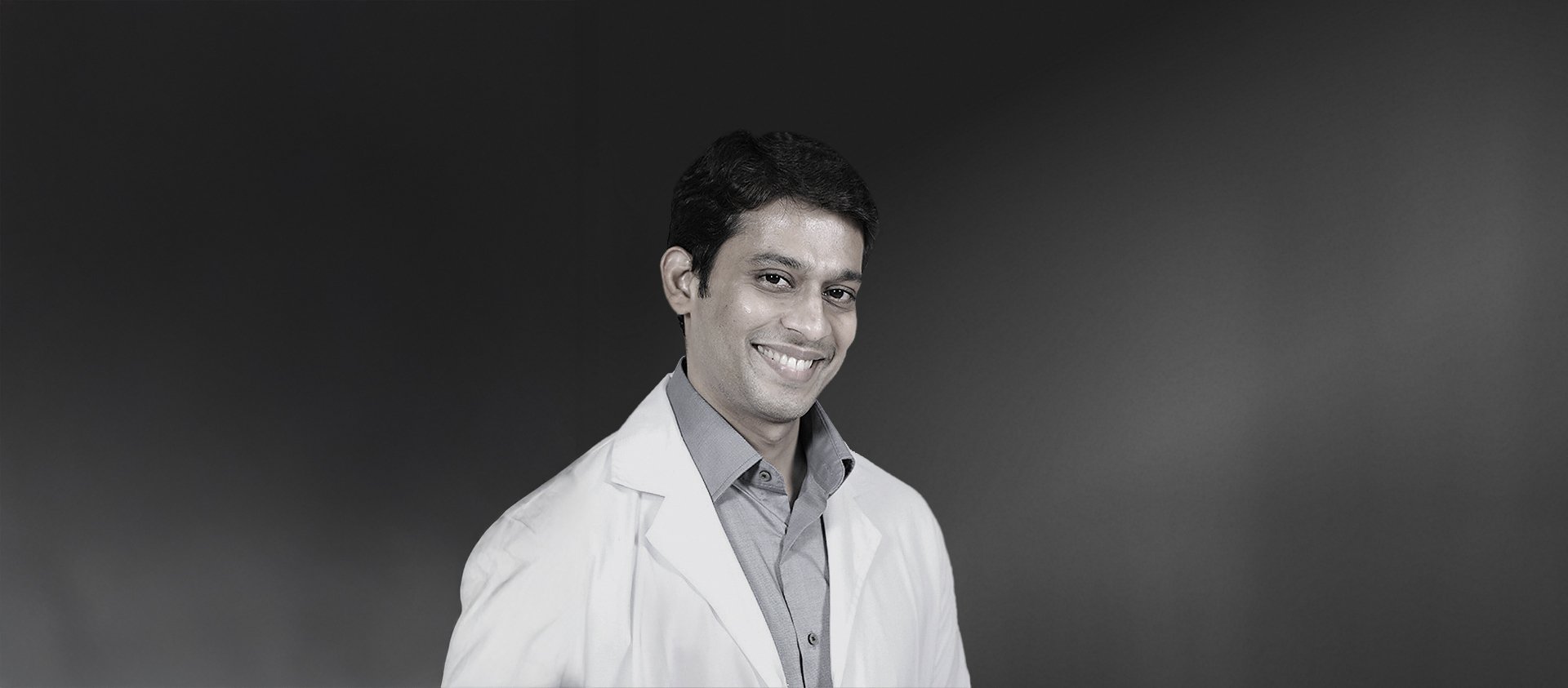 Smiling ophthalmologist Dr Sherren Raveendran from Ain Al Khaleej Hospital United Arab Emirates in white medical coat against dark background