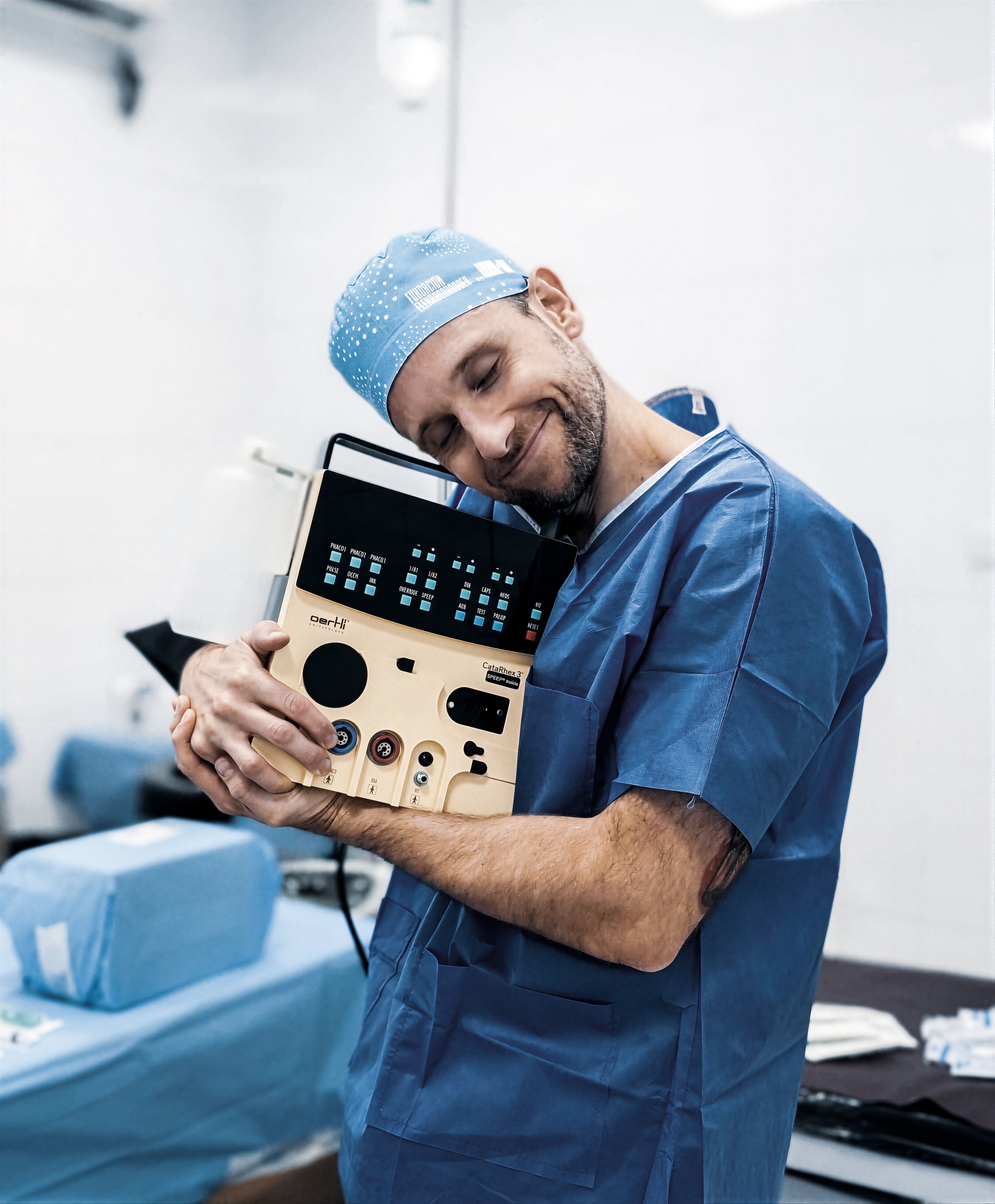 Smiling ophthalmic surgeon embracing a CataRhex 3 surgical platform in an operating room during a charitable eye care mission