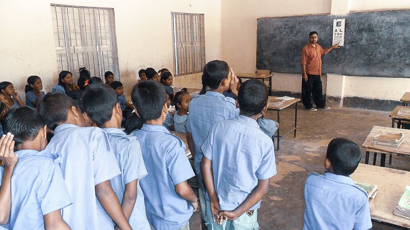 Teacher conducting a vision screening with schoolchildren in a classroom using an eye chart