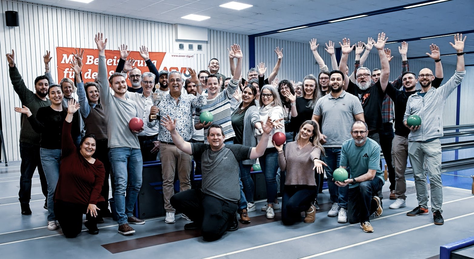 Oertli Mitarbeitende posieren gemeinsam bei einem Bowling-Event und winken gut gelaunt in die Kamera