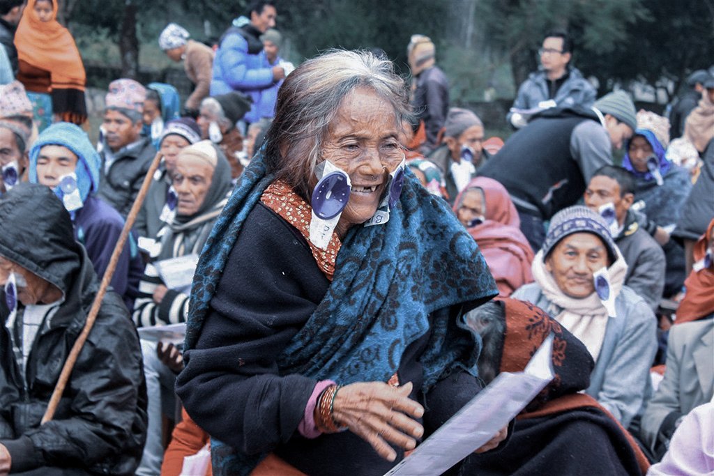 People waiting during an eye care outreach programme, with an elderly woman holding paperwork in the foreground