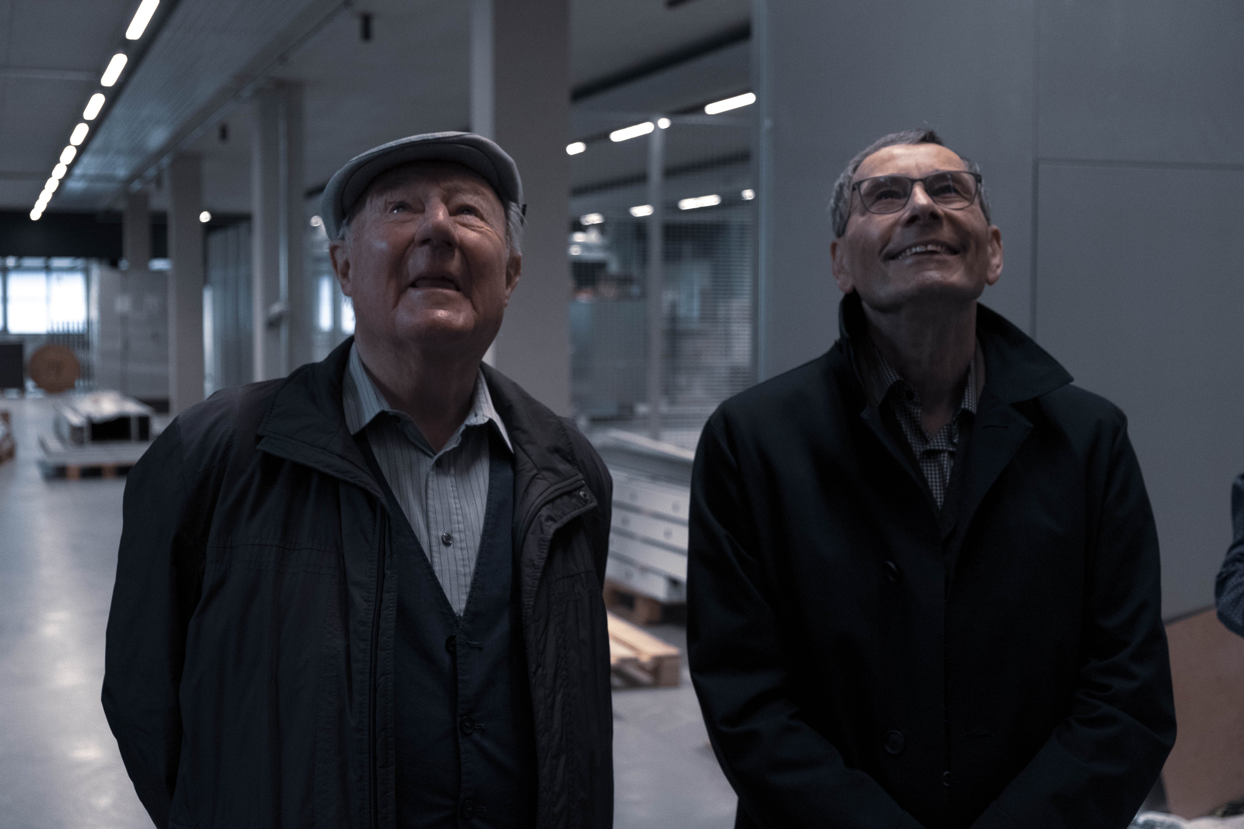 Two men (lheinz oertli and andreas bosshard) look upwards while standing inside a modern production and logistics facility
