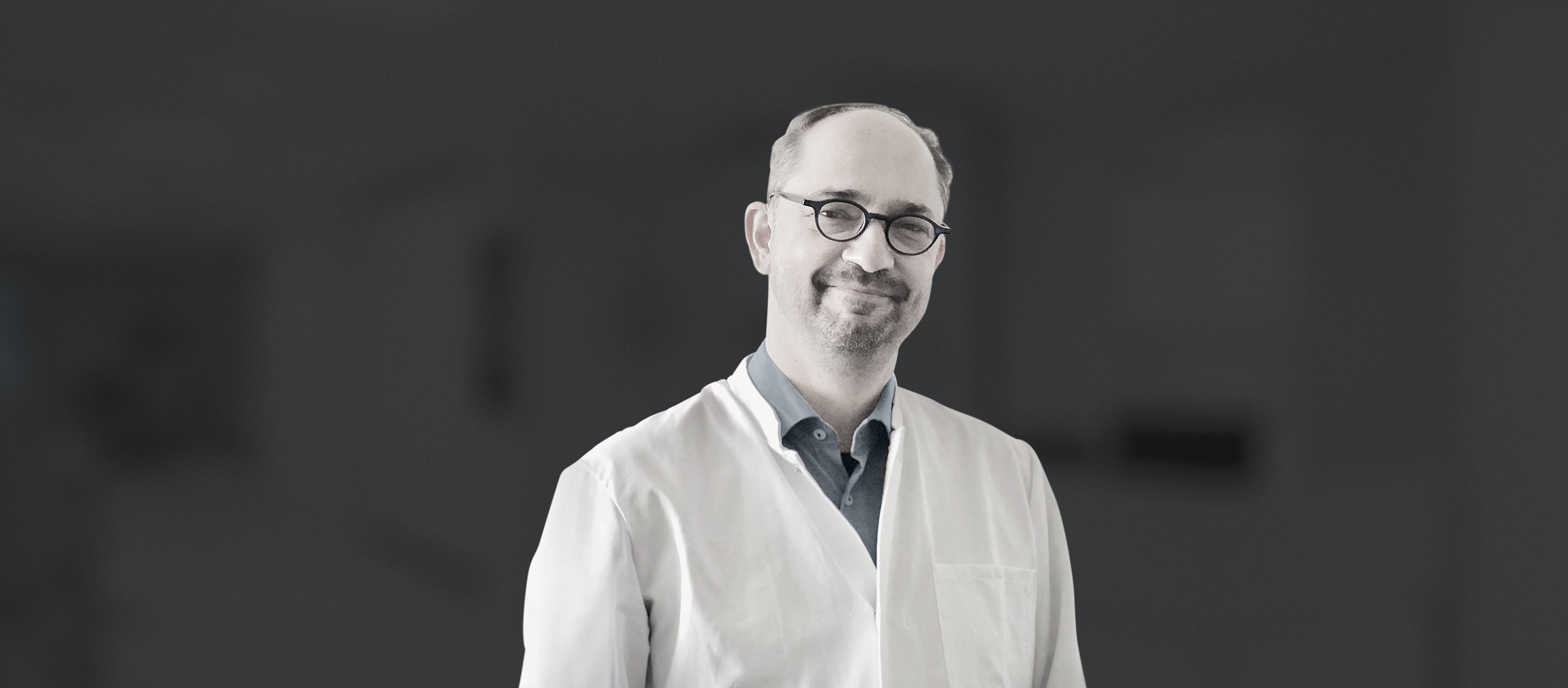 Portrait of ophthalmologist in clinical setting, wearing white coat and glasses, smiling against softly blurred background
