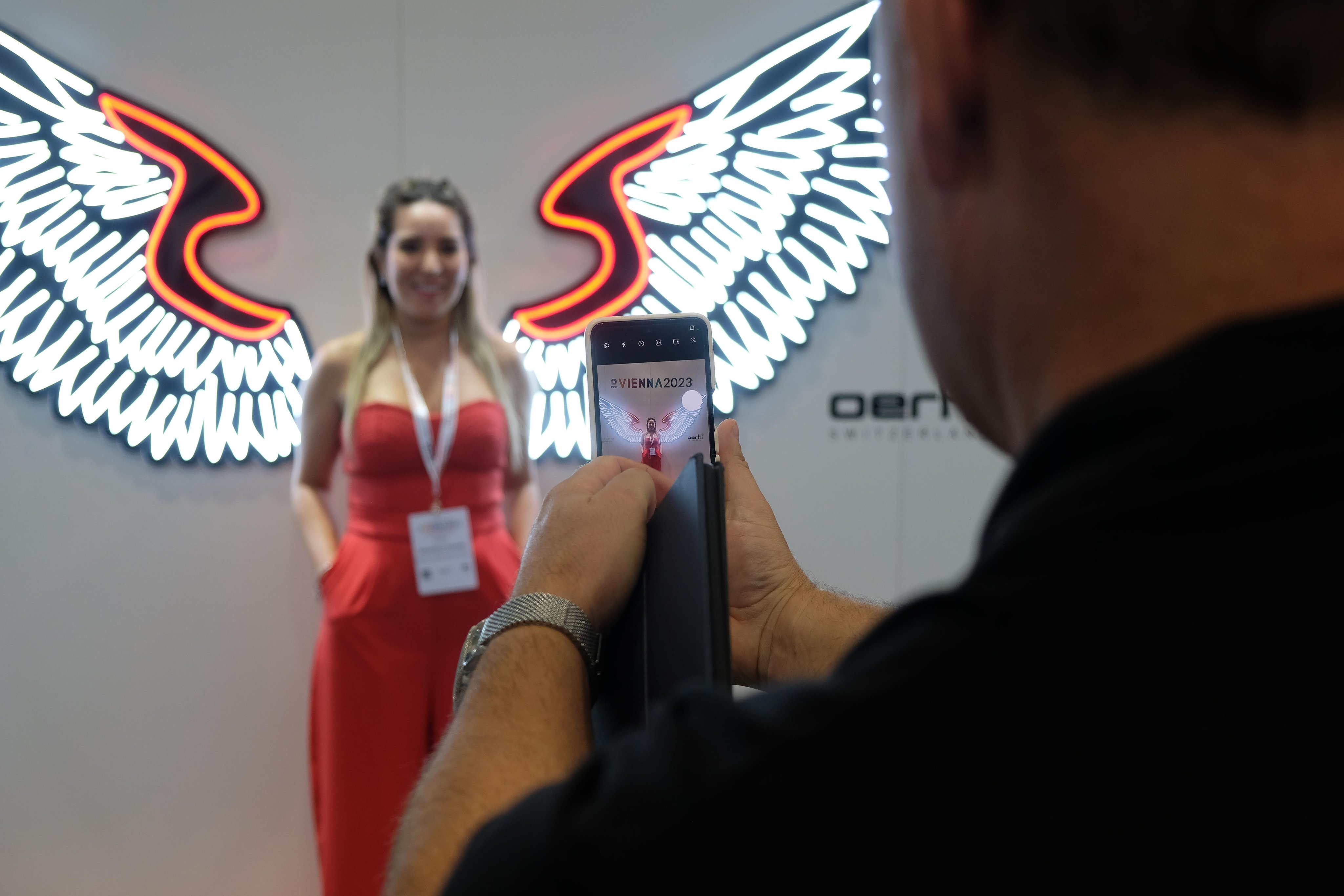 Visitor taking a photo at the Oertli booth during ESCRS 2023, with illuminated wings and Oertli branding in the background
