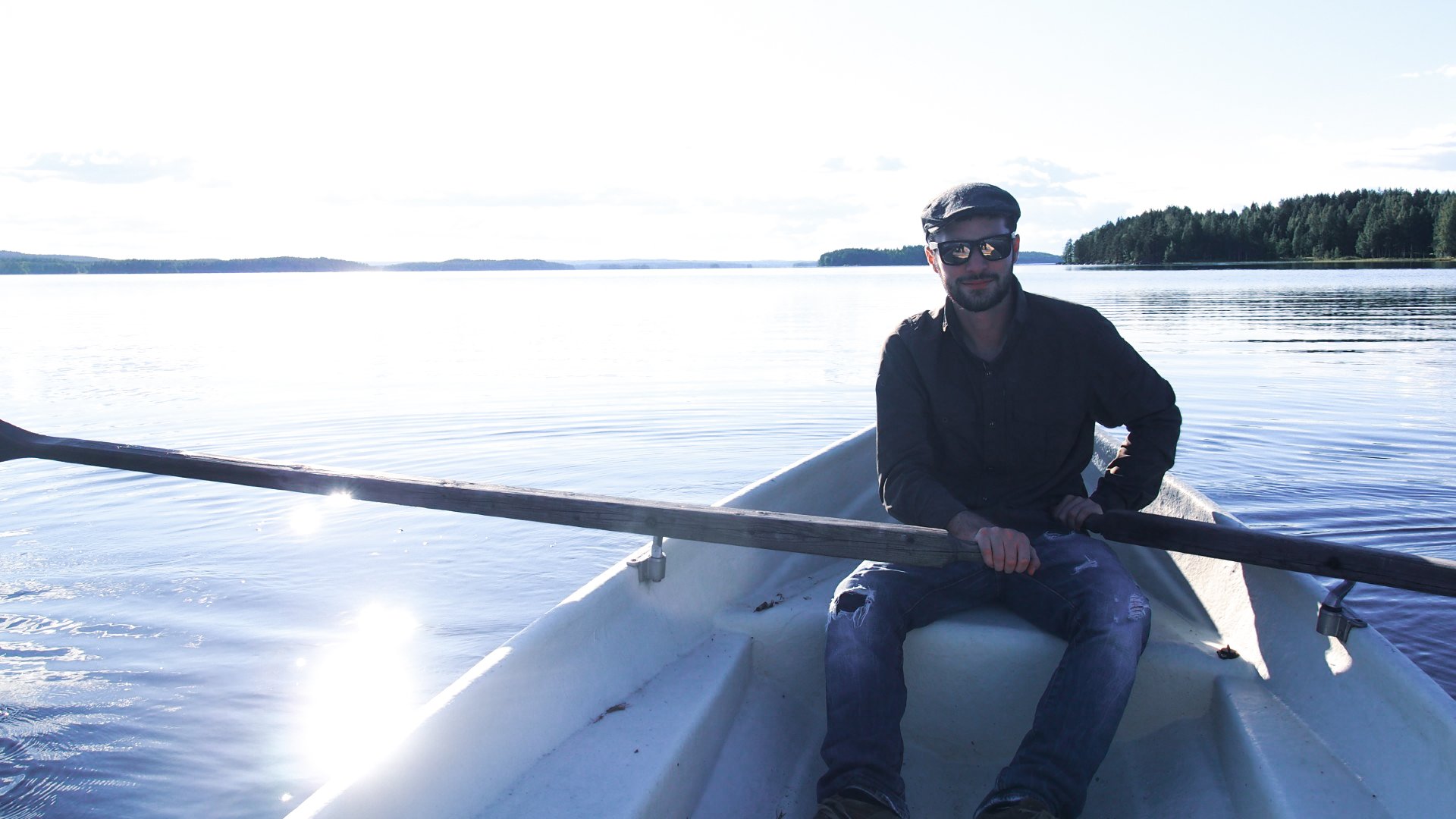 Ein Mann sitzt in einem Ruderboot auf einem ruhigen See und hält die Ruder in den Händen