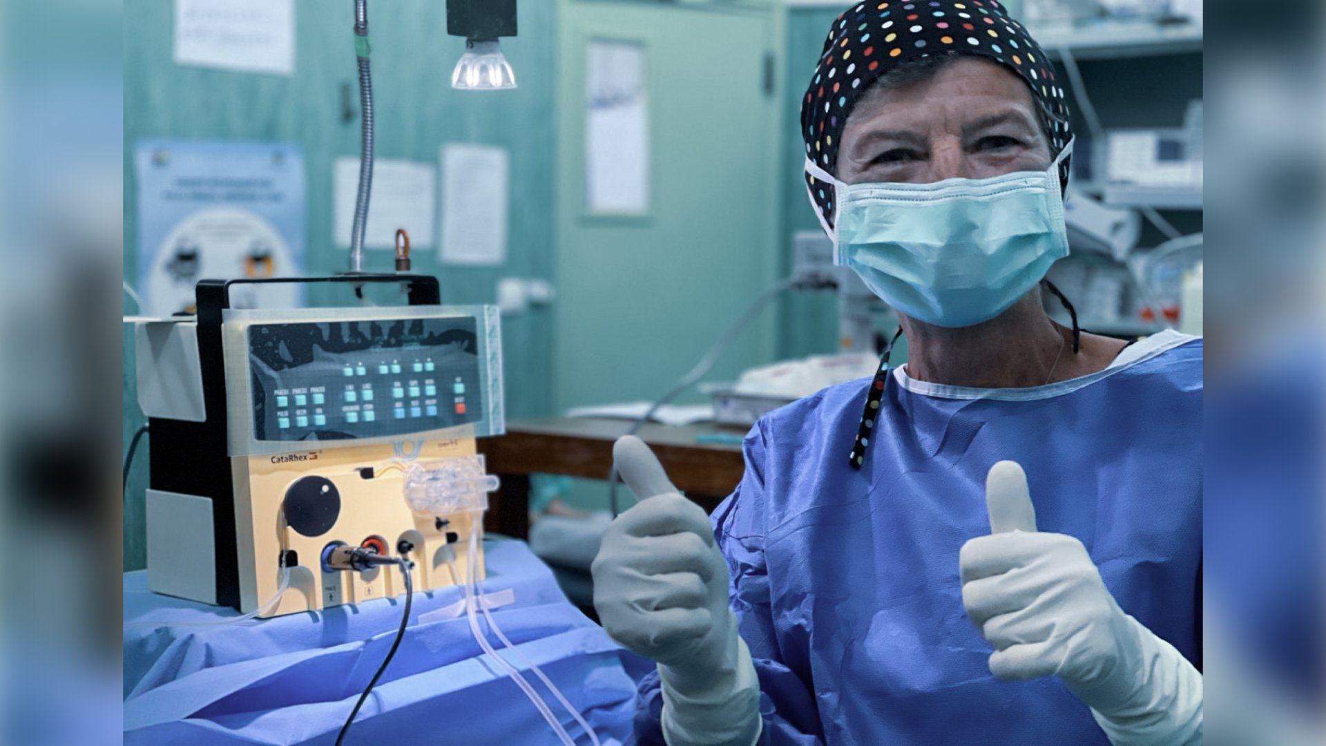 Eye surgeon in an operating theatre giving a thumbs up next to a portable CataRhex 3 cataract surgery system during an outreach eye care mission