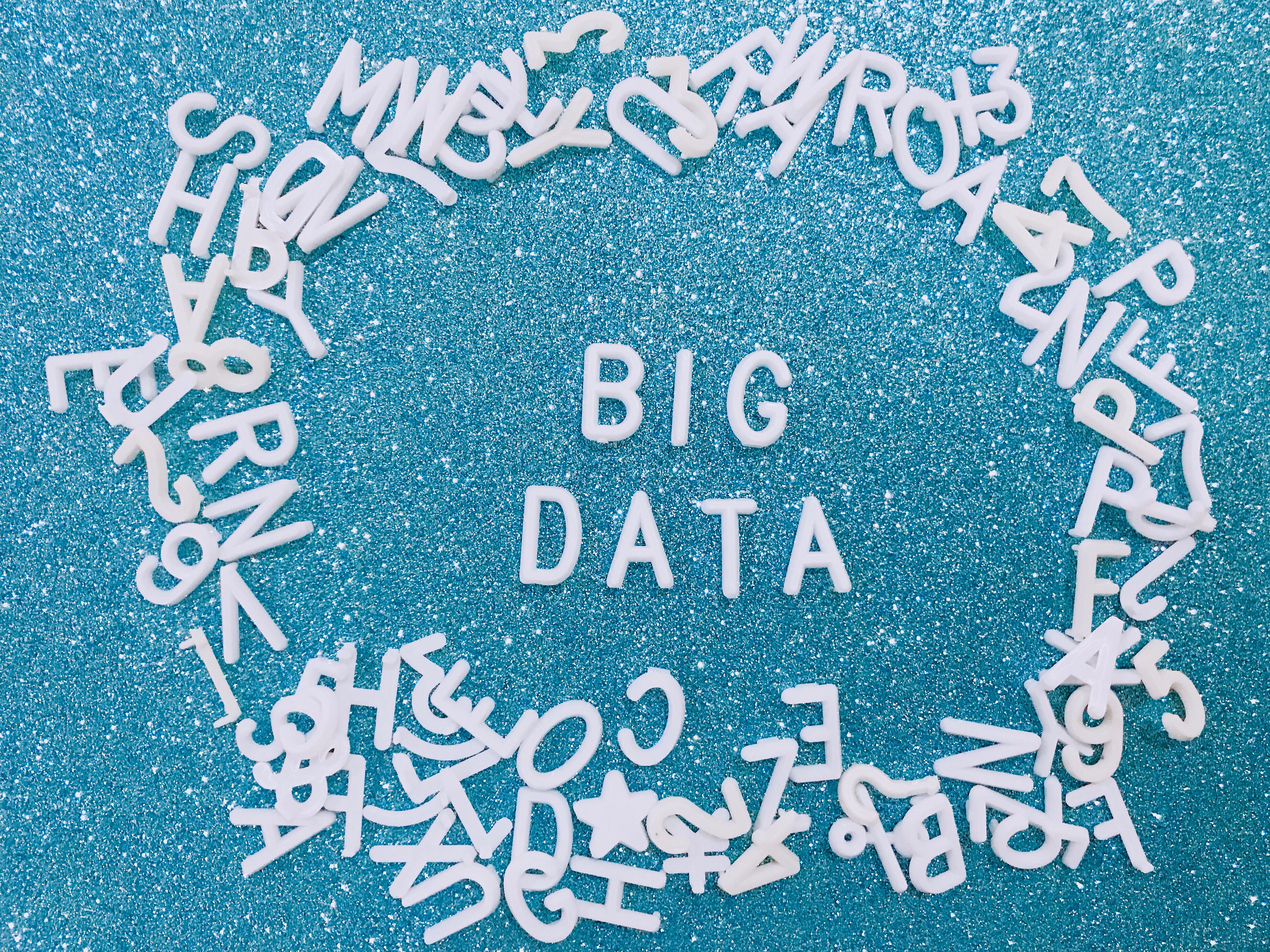 “Big Data” lettering surrounded by scattered white letters on a blue background, symbolising data volume and digital information