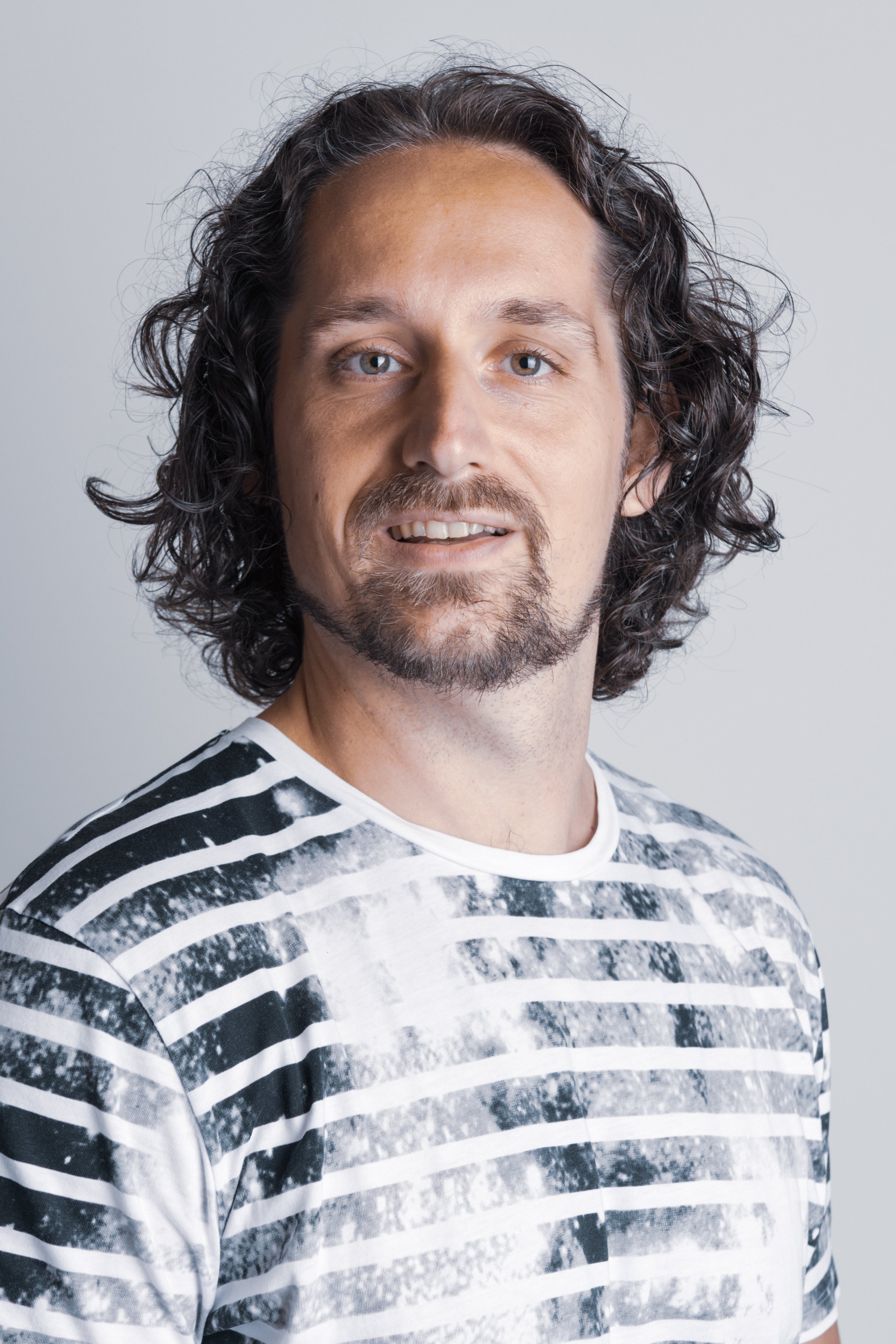 Professional portrait of a smiling Oertli employee with curly dark hair and a striped shirt