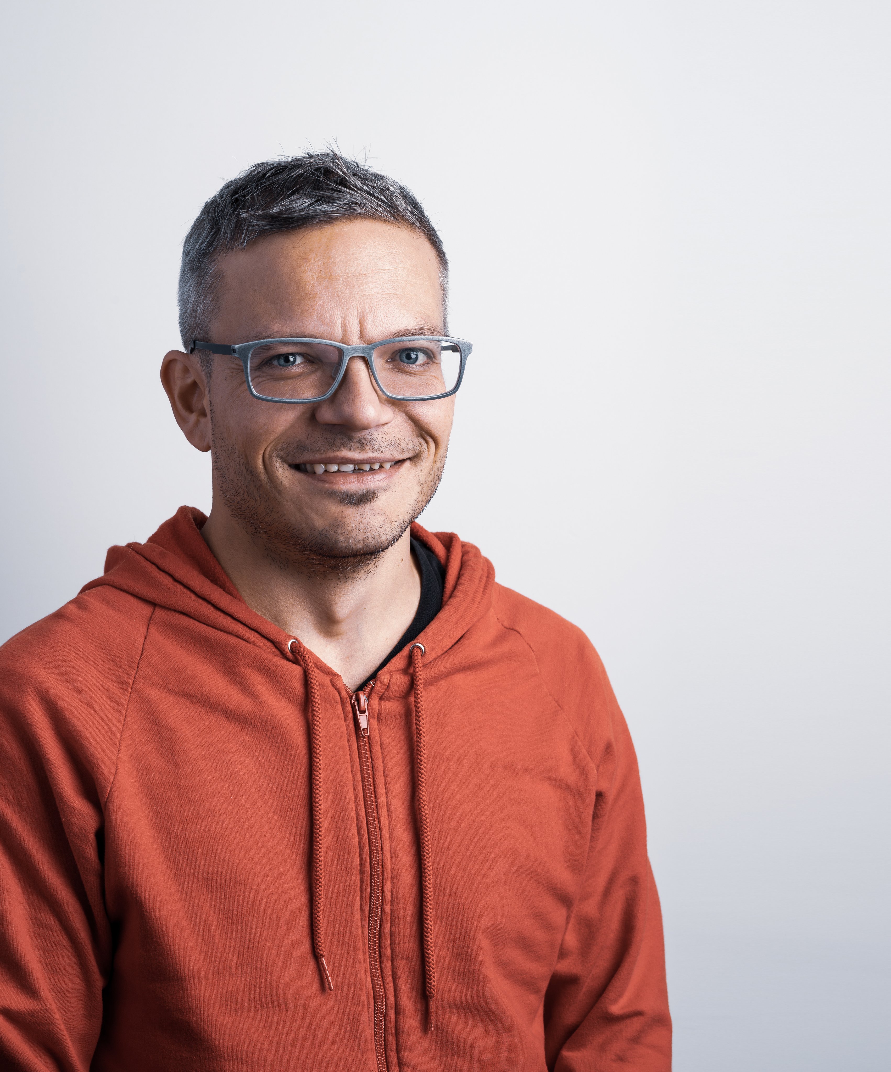 Professional portrait of a smiling Oertli employee wearing glasses and a rust-coloured hoodie