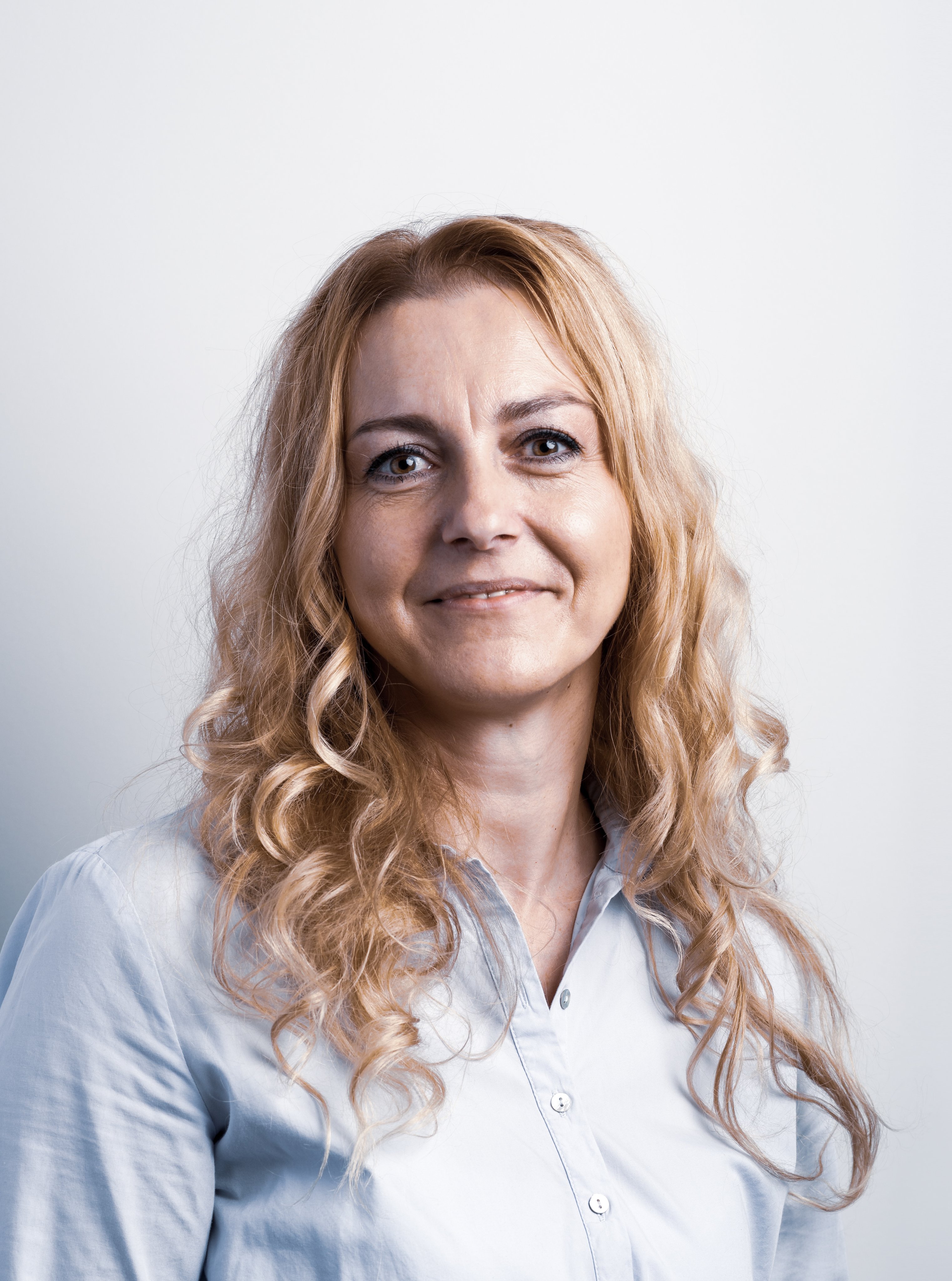 Professional portrait of a smiling Oertli employee with curly blonde hair and a light blue shirt