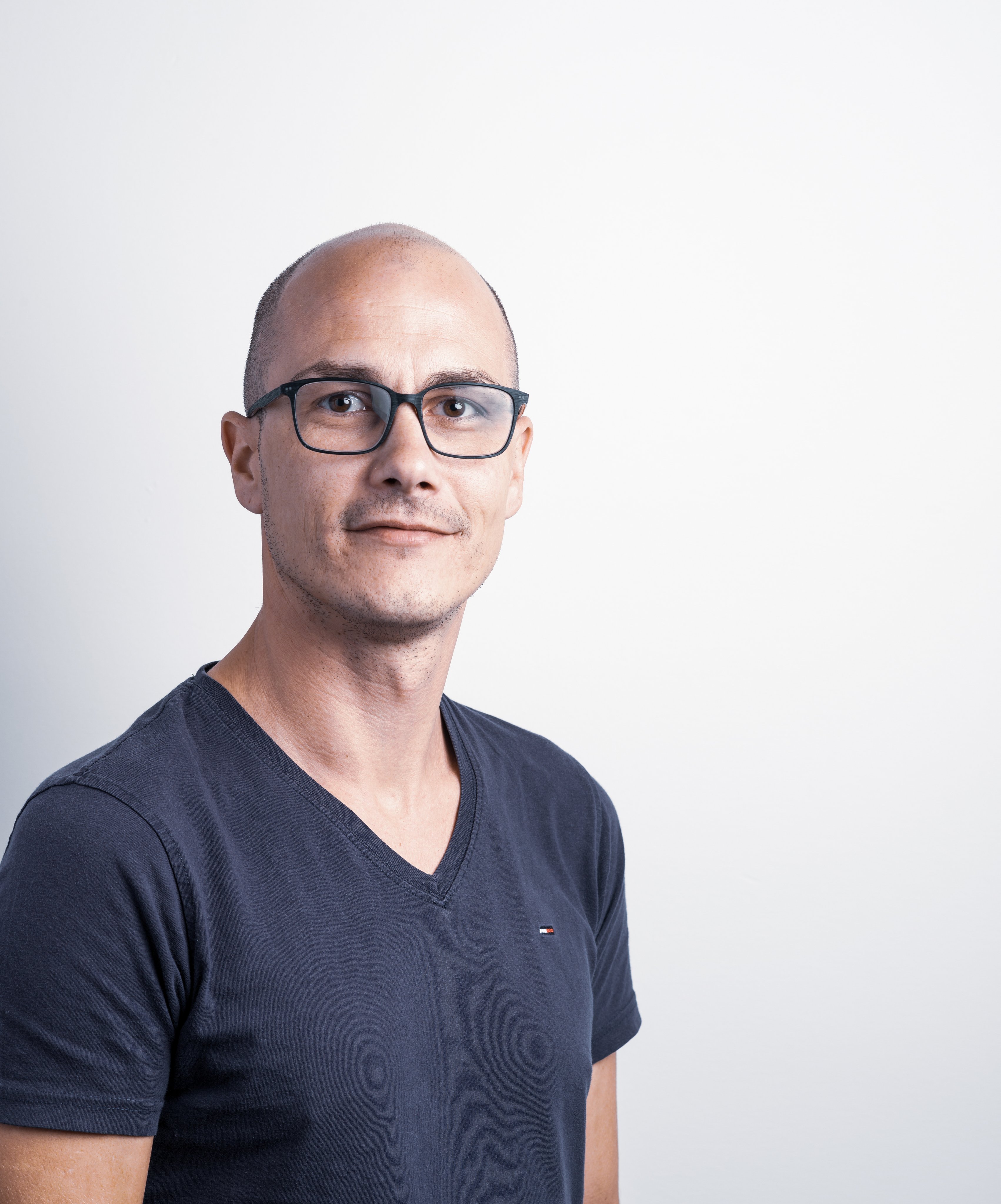 Professional portrait of an Oertli employee wearing glasses and a dark T-shirt