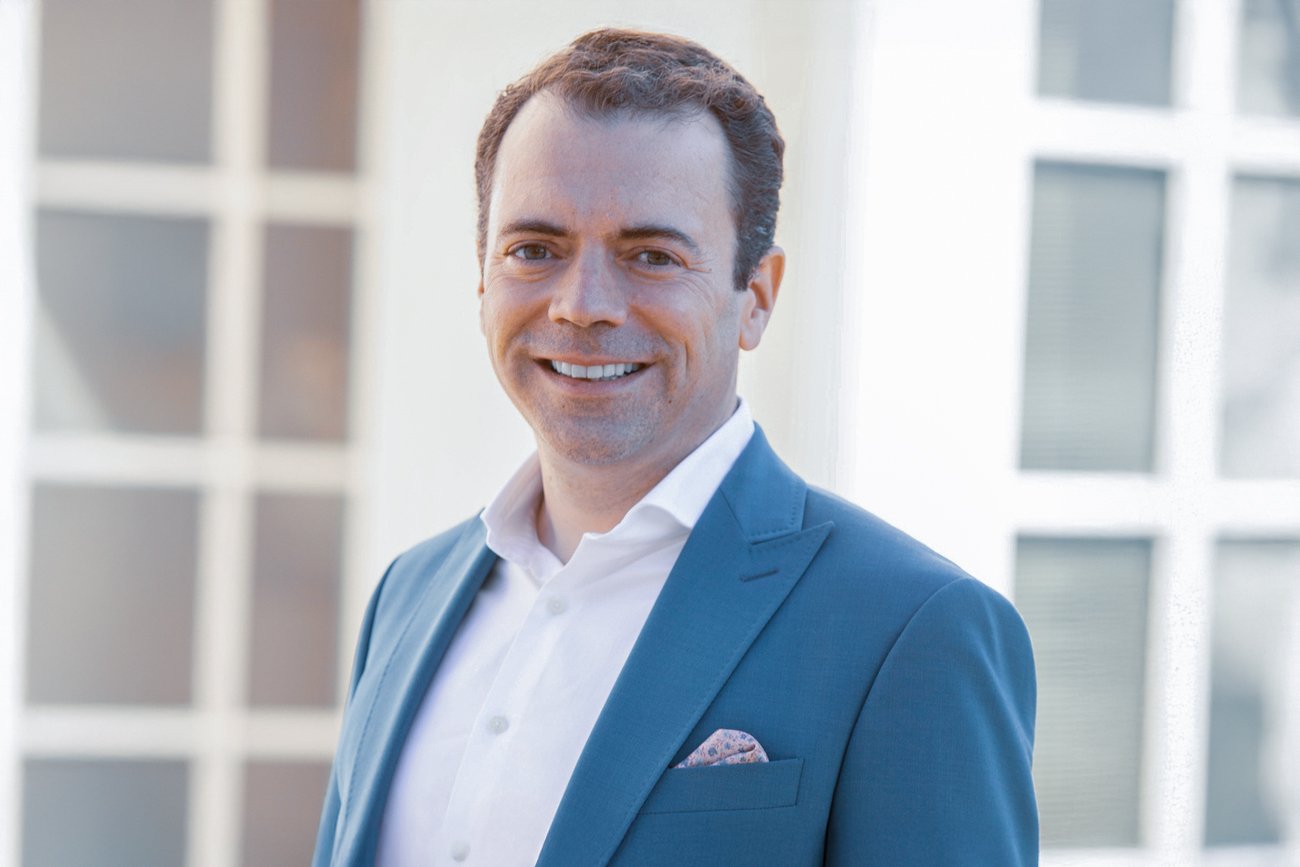 Portrait of a smiling ophthalmologist in a blue suit jacket against a bright urban background