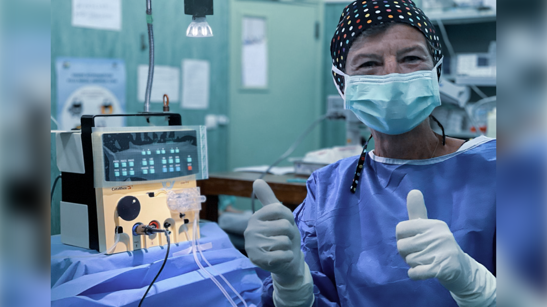 Eye surgeon in an operating theatre giving a thumbs up next to a portable CataRhex 3 cataract surgery system during an outreach eye care mission