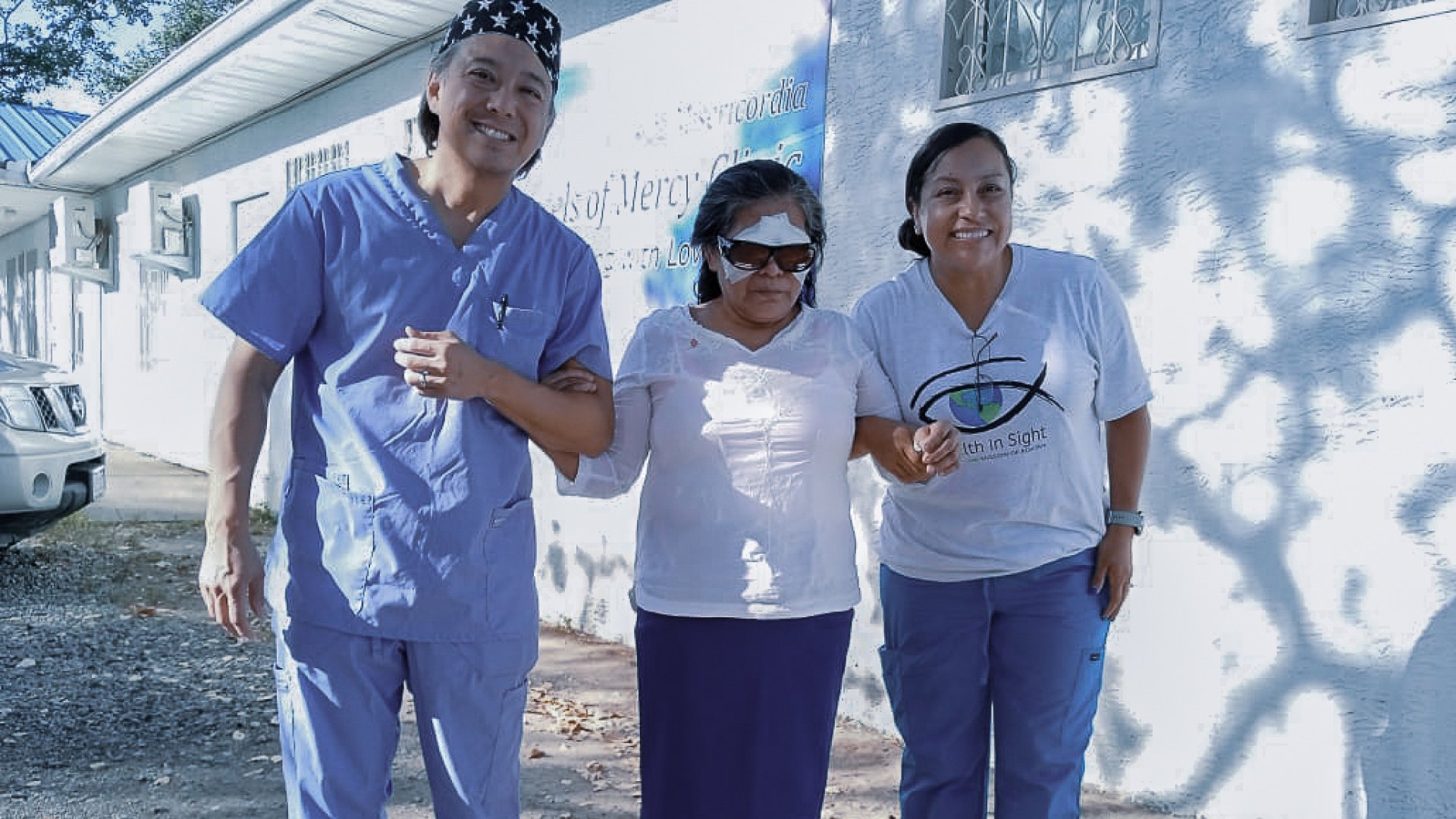 Healthcare volunteers walking with a patient outside an eye care facility after receiving ophthalmic treatment