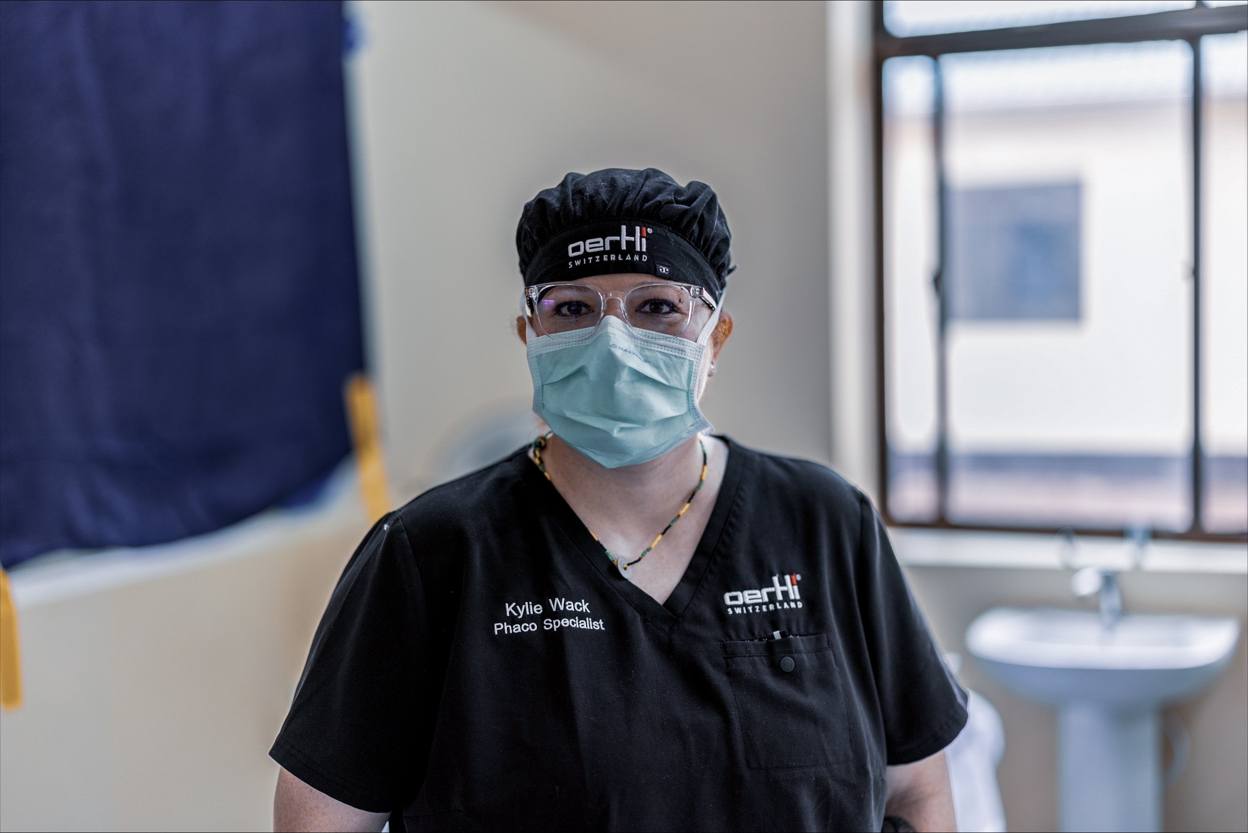 Oertli phaco specialist wearing surgical scrubs, mask, safety glasses and cap in a clinical setting