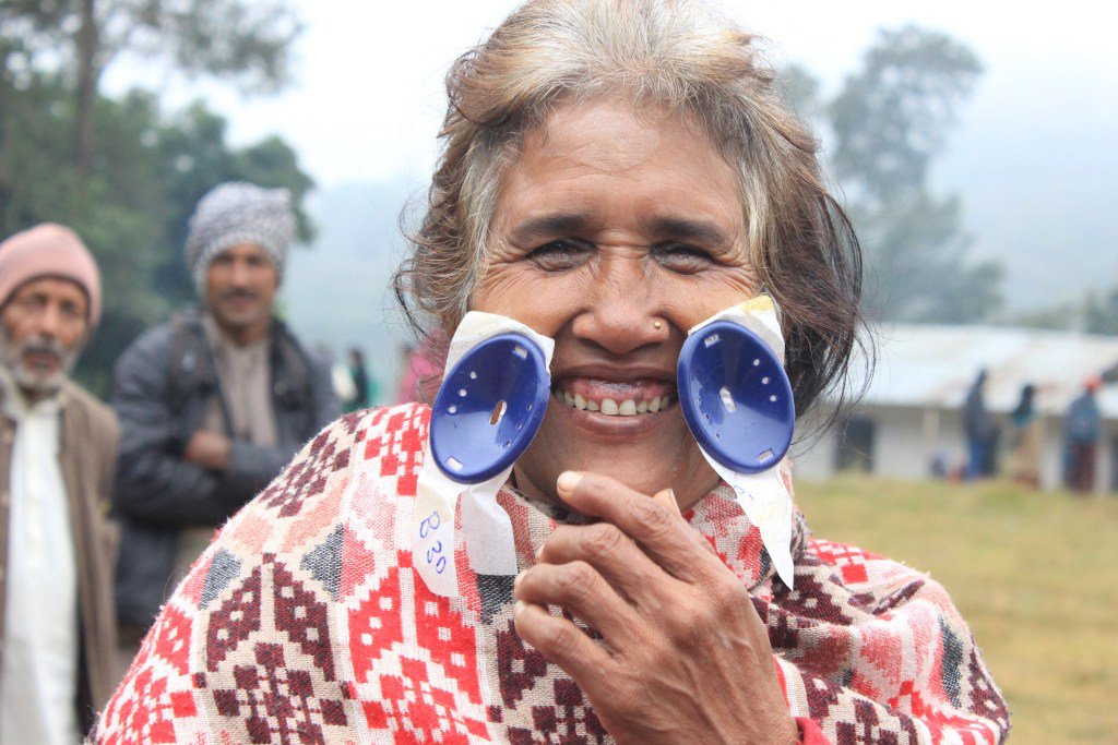 Woman smiling while holding ophthalmic devices during an eye care outreach programme, highlighting access to cataract treatment and vision care in a rural community