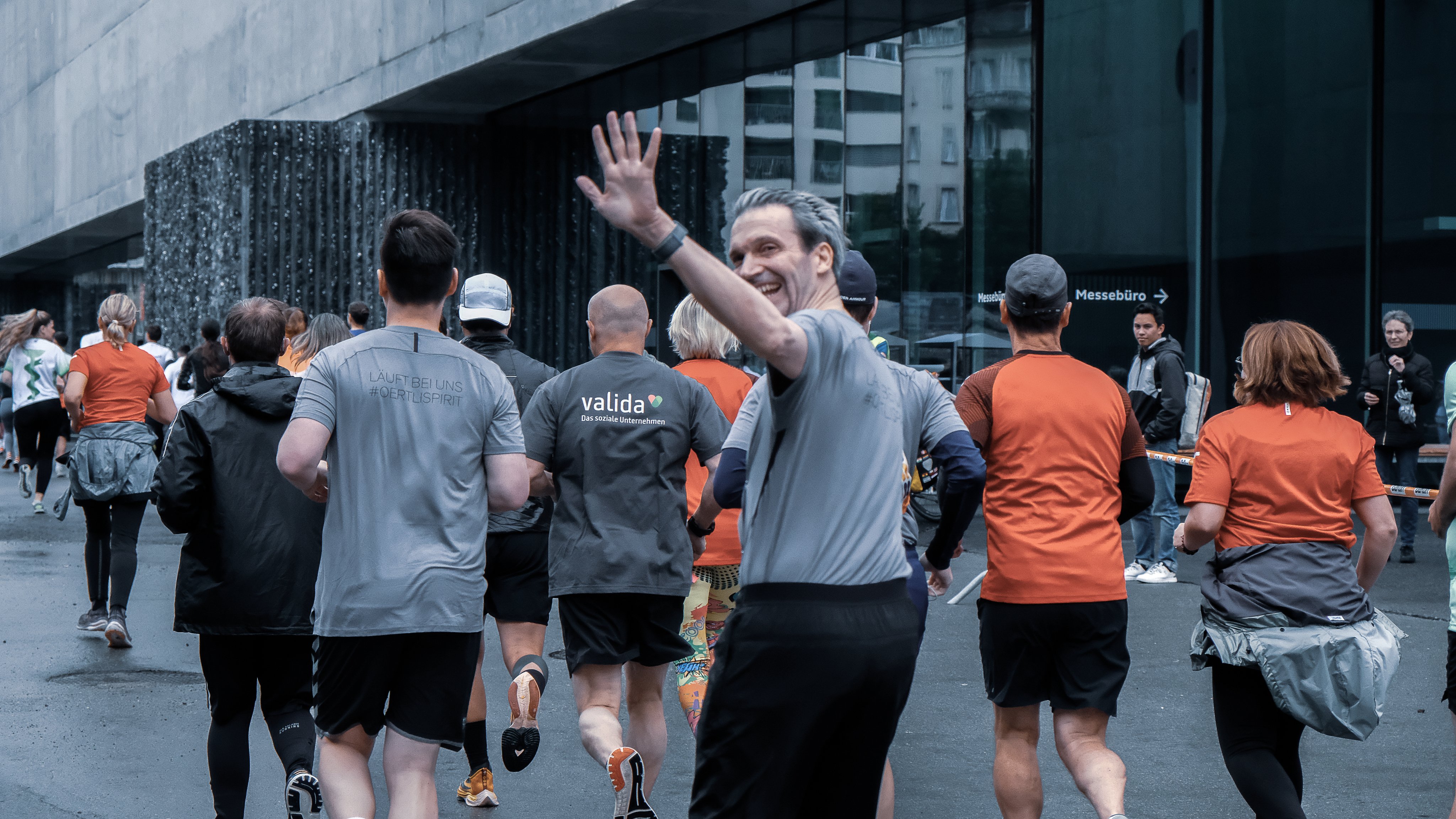 Oertli Mitarbeitende laufen gemeinsam am B2Run, ein Teilnehmer dreht sich lächelnd zur Kamera und winkt