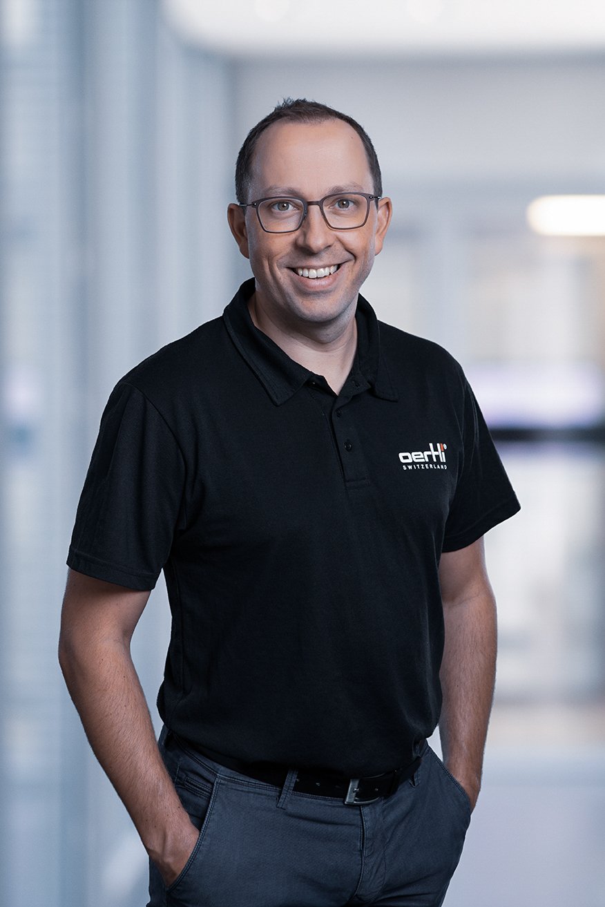 Portrait of a smiling Oertli CEO wearing a black Oertli shirt in a bright office setting