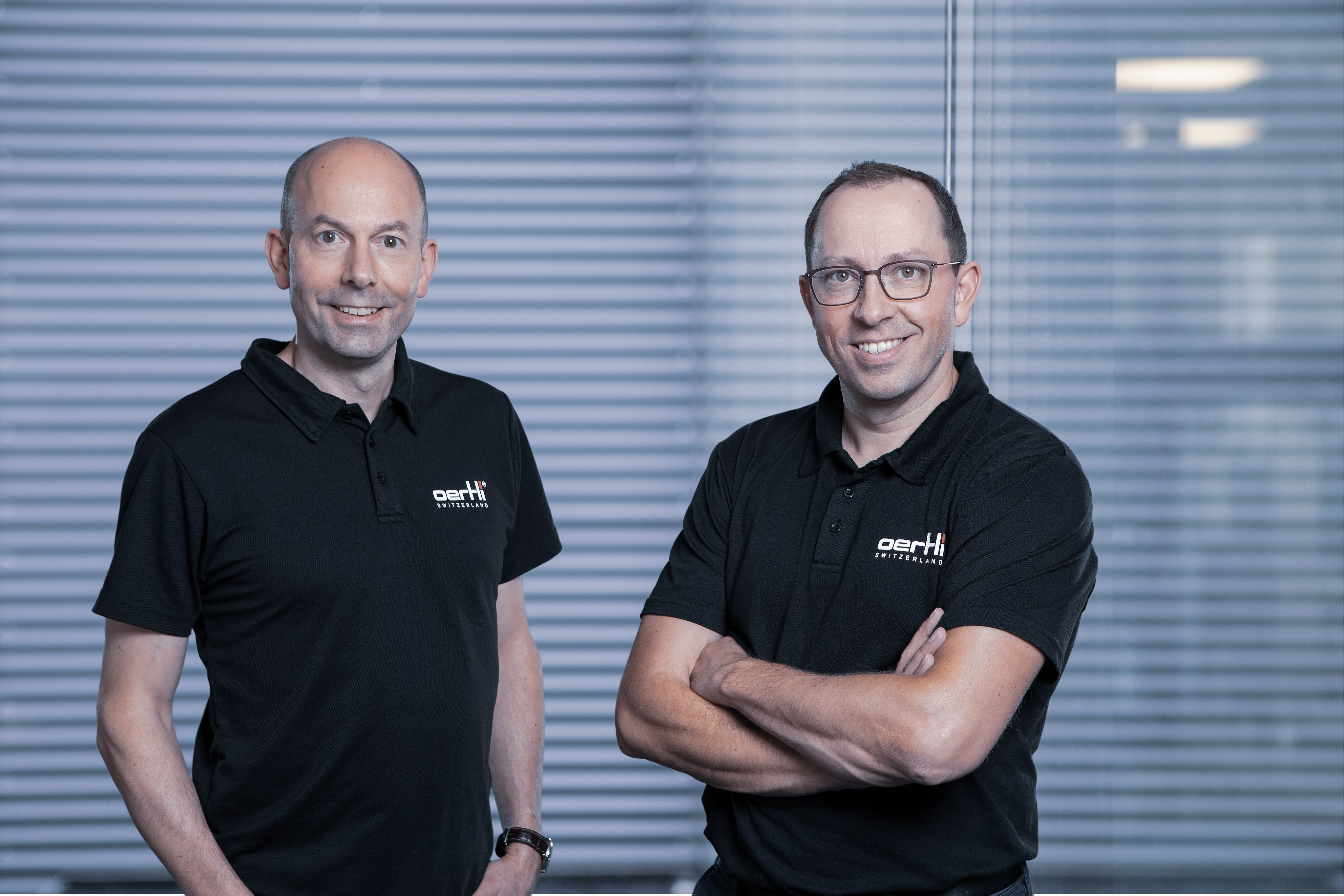 Portrait of smiling Christoph and Thomas Bosshard, brothers and CEOs of Oertli, wearing black company polo shirts
