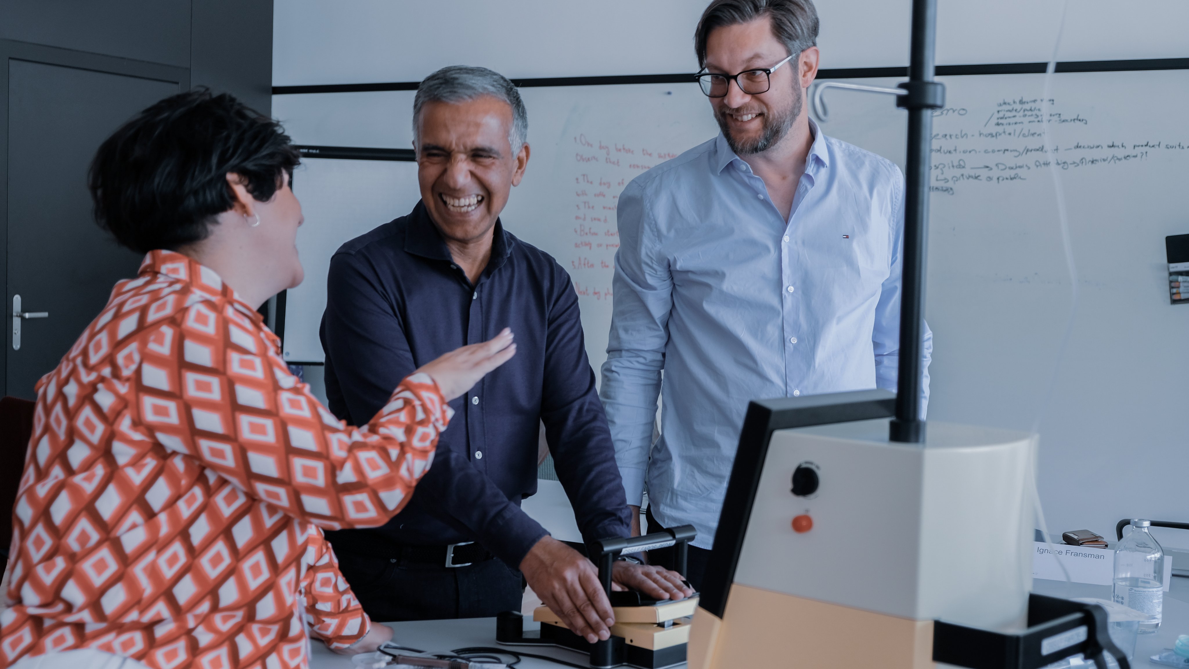 Three participants engaged in a sales and application training session, discussing and interacting with ophthalmic surgical equipment in a classroom setting