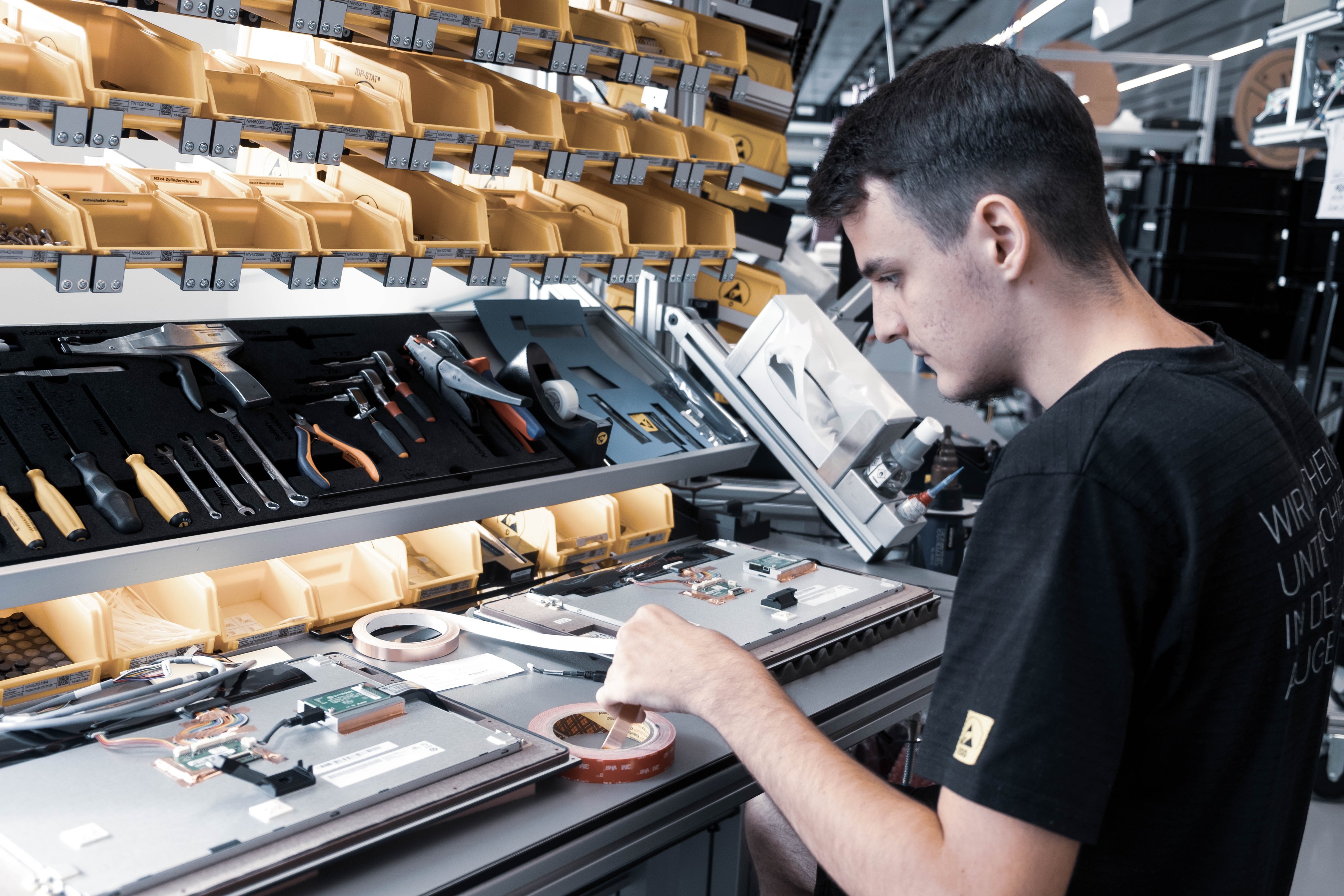 Mitarbeitender arbeitet an der Montage von elektronischen Komponenten an einem Werkbankplatz
