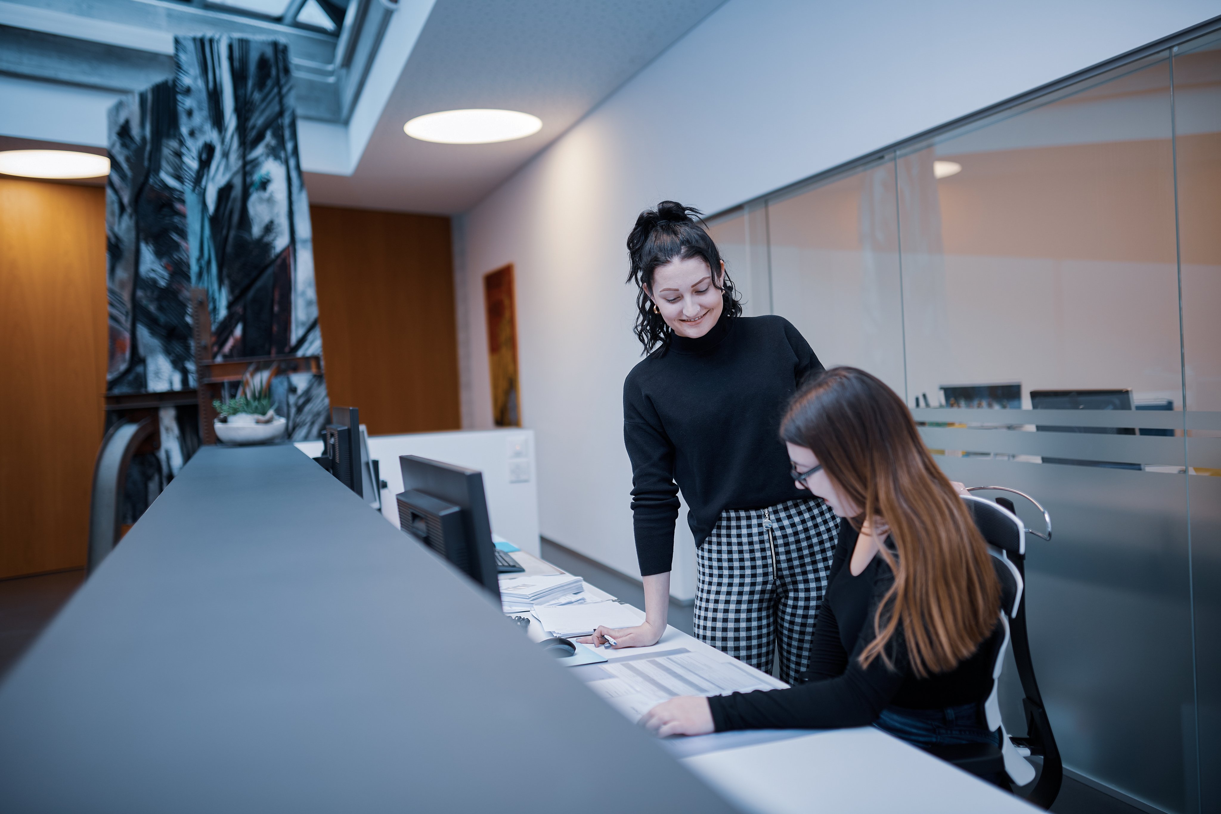 Zwei Mitarbeitende besprechen Dokumente an einem Computerarbeitsplatz an Empfang
