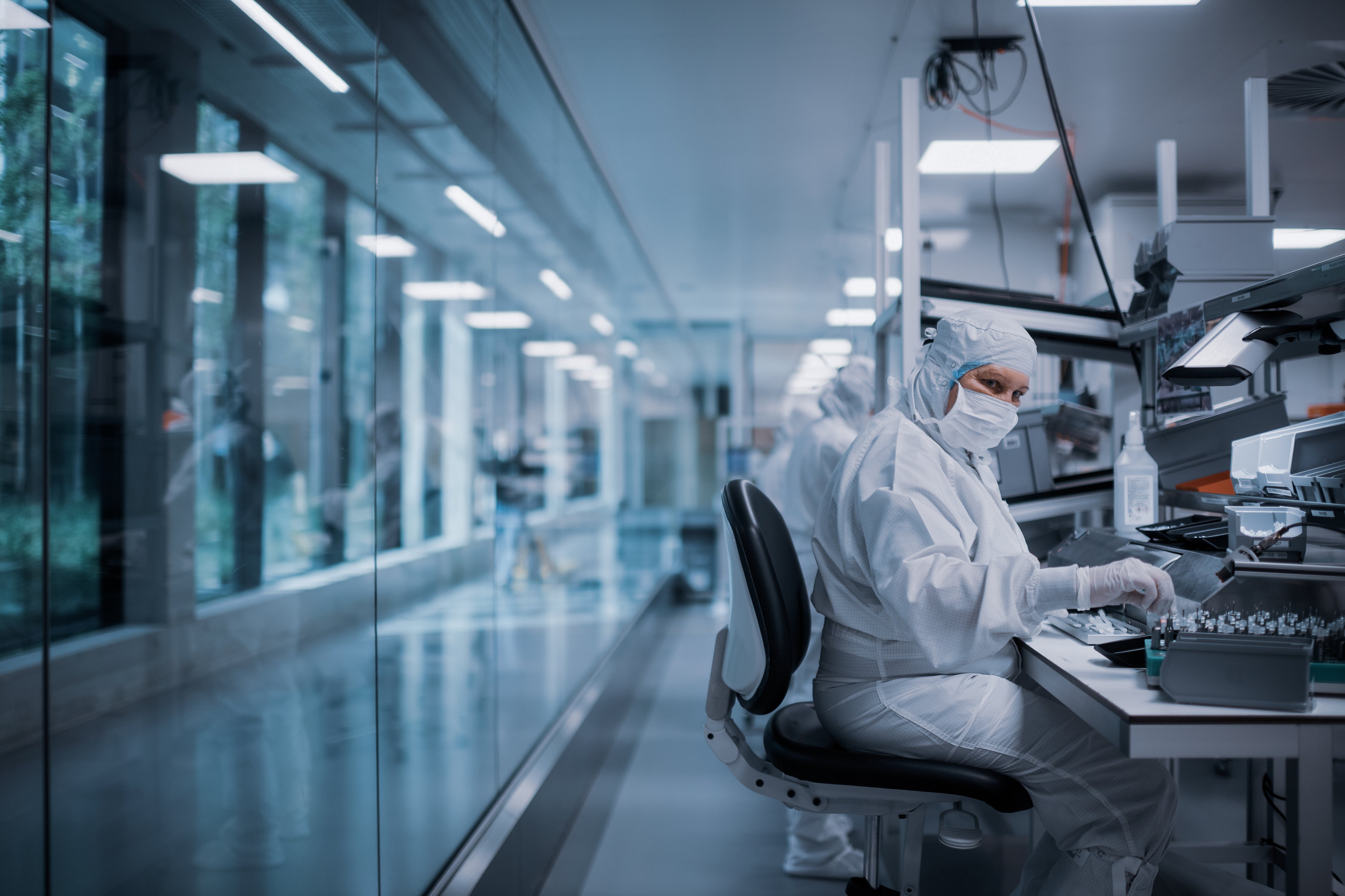 Cleanroom employee in protective clothing assembling and inspecting ophthalmic surgical components at a workstation