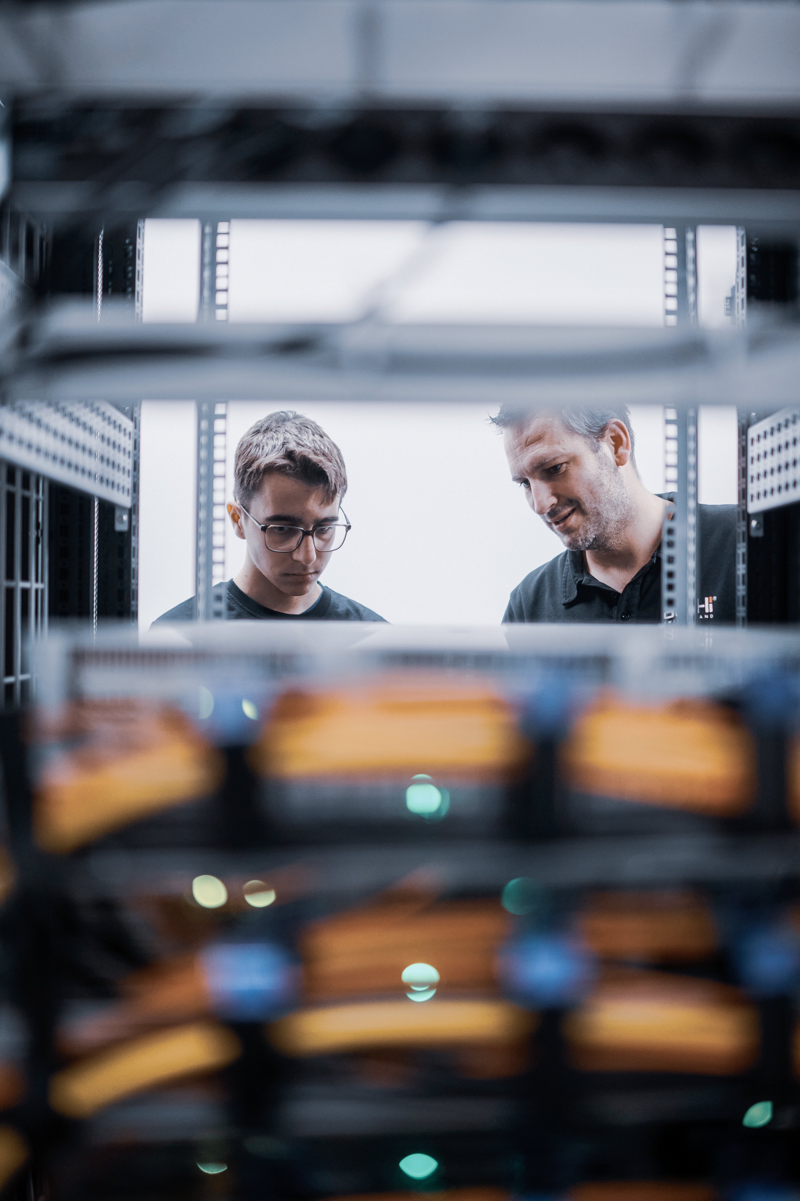 Oertli employee guiding an apprentice while inspecting technical equipment in a training workspace