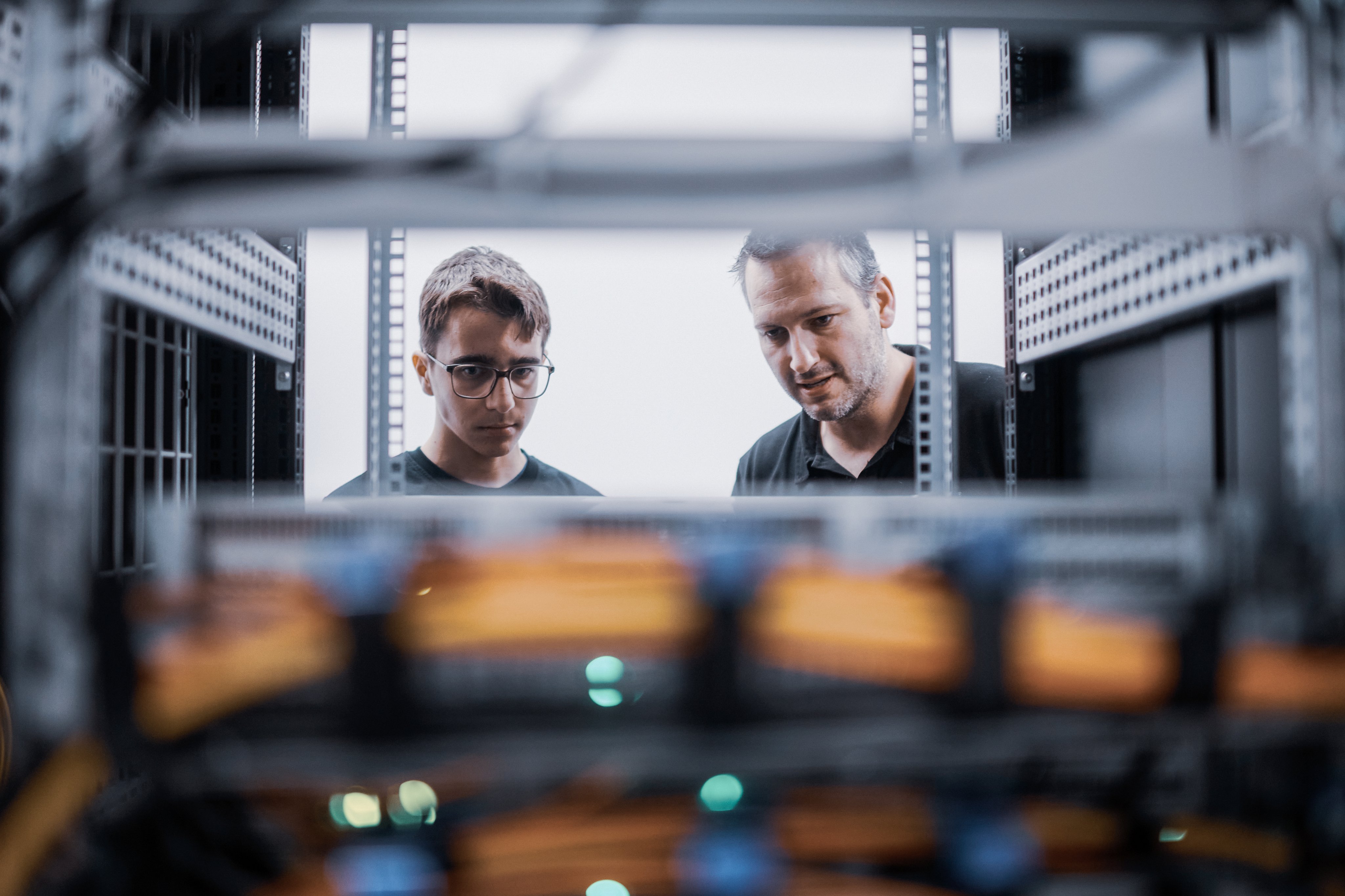 Lehrmeister instruiert den Lernenden bei seiner Aufgabe vor dem IT-Serverraum