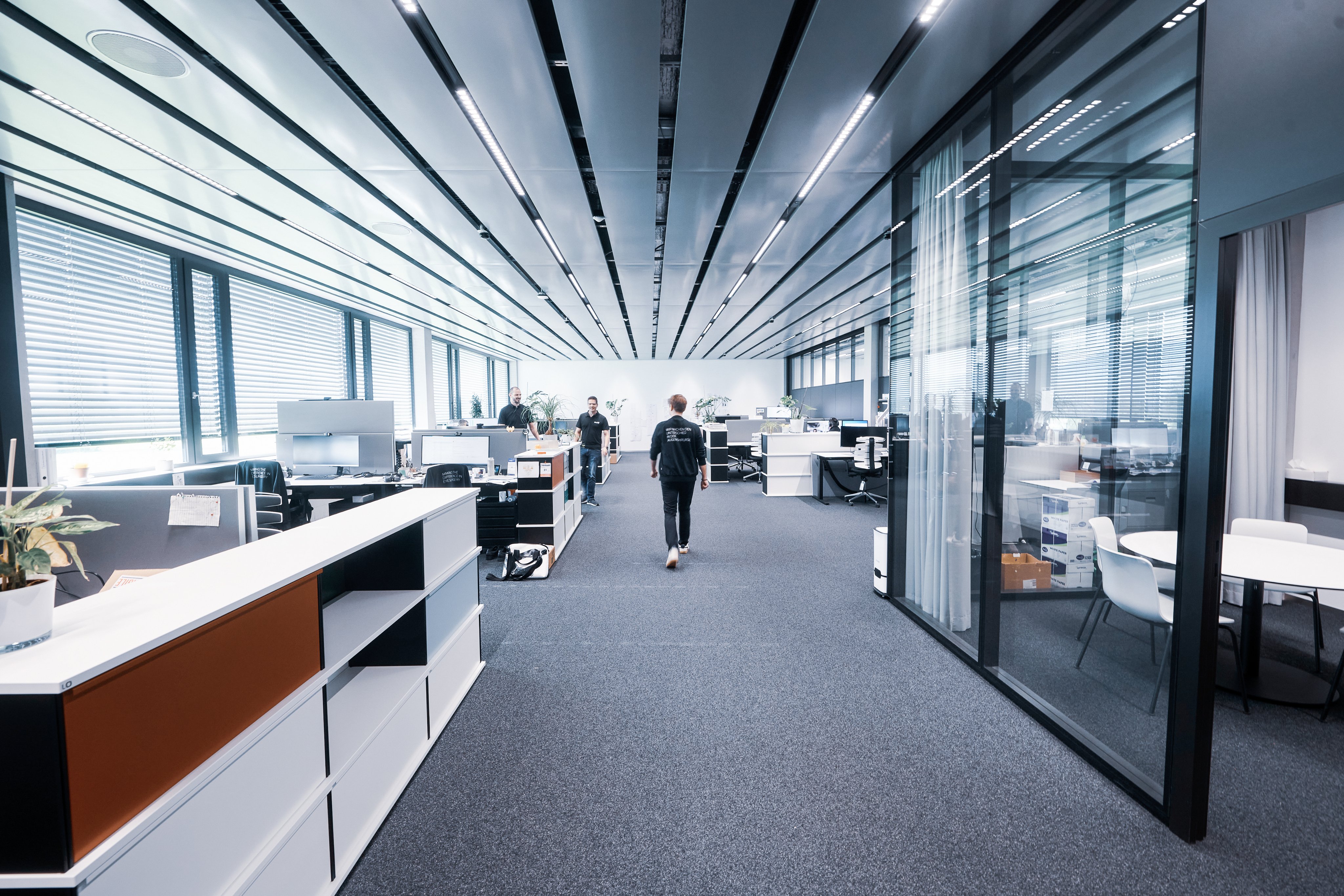 Offener Bürobereich mit Arbeitsplätzen und Mitarbeitenden in einem modernen Unternehmen