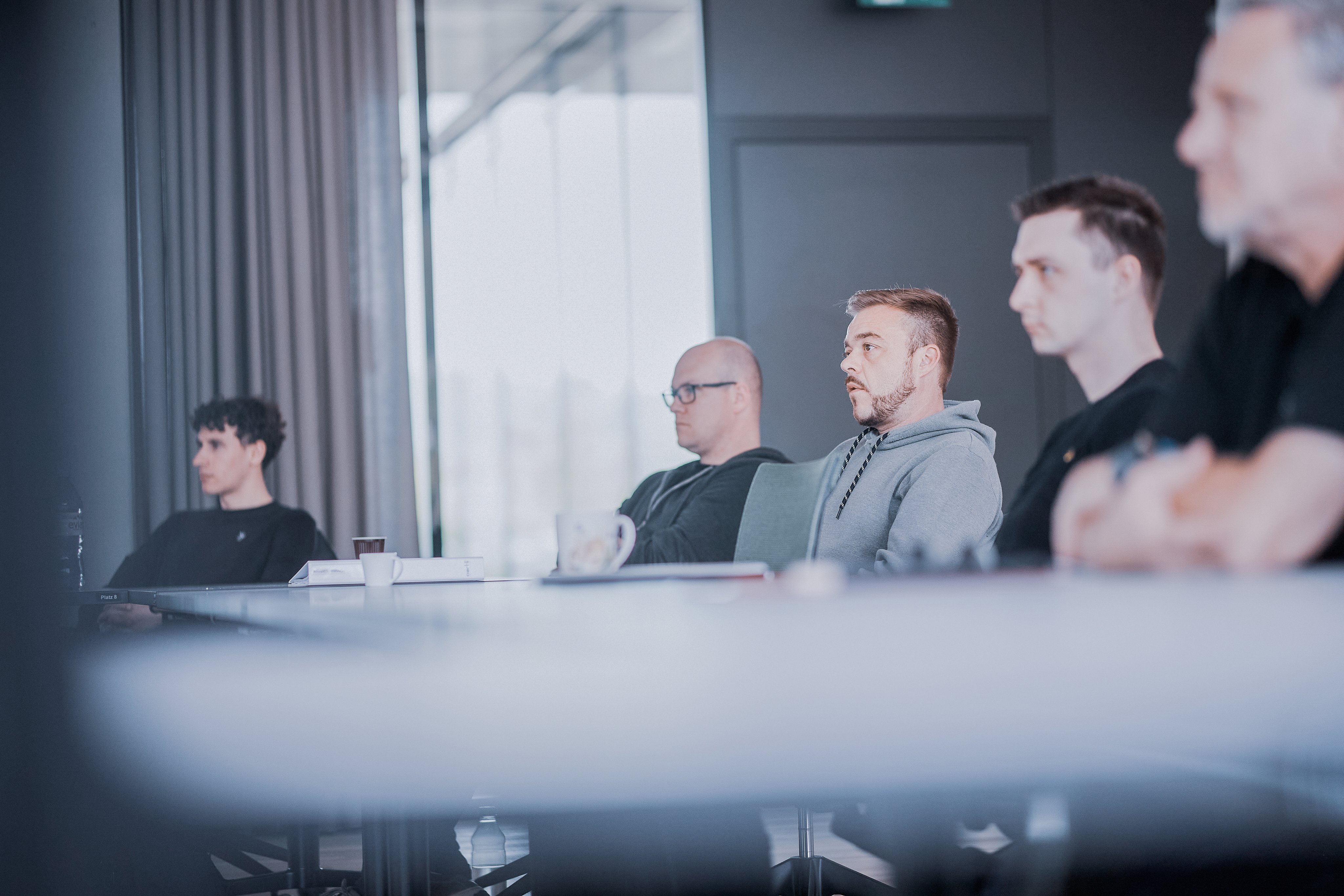 Mehrere Mitarbeitende sitzen in einem modernen Sitzungsraum an einem Besprechungstisch und verfolgen aufmerksam eine Präsentation