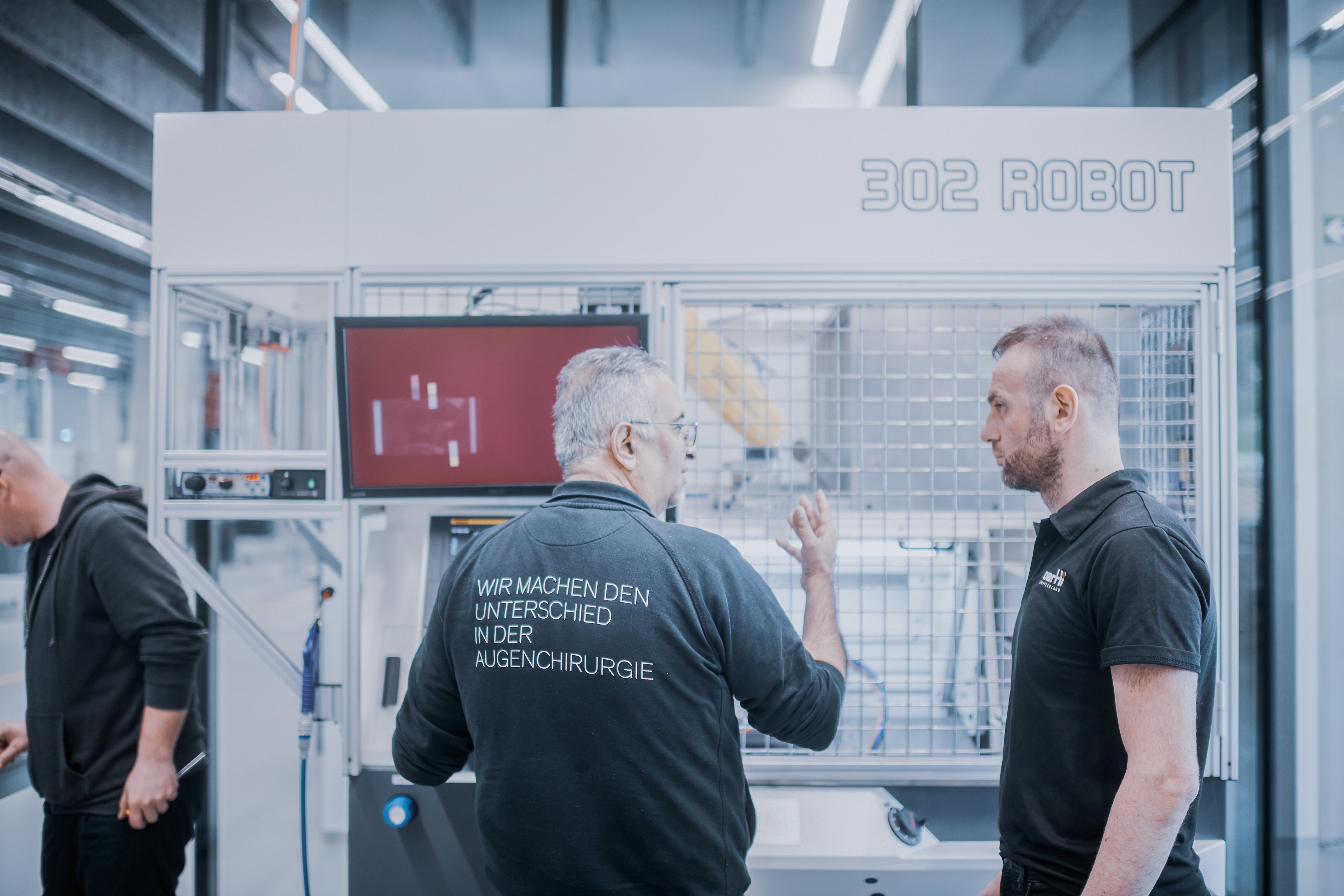 Mitarbeitende diskutieren einen automatisierten Fertigungsprozess vor einer Roboterzelle in der Produktion