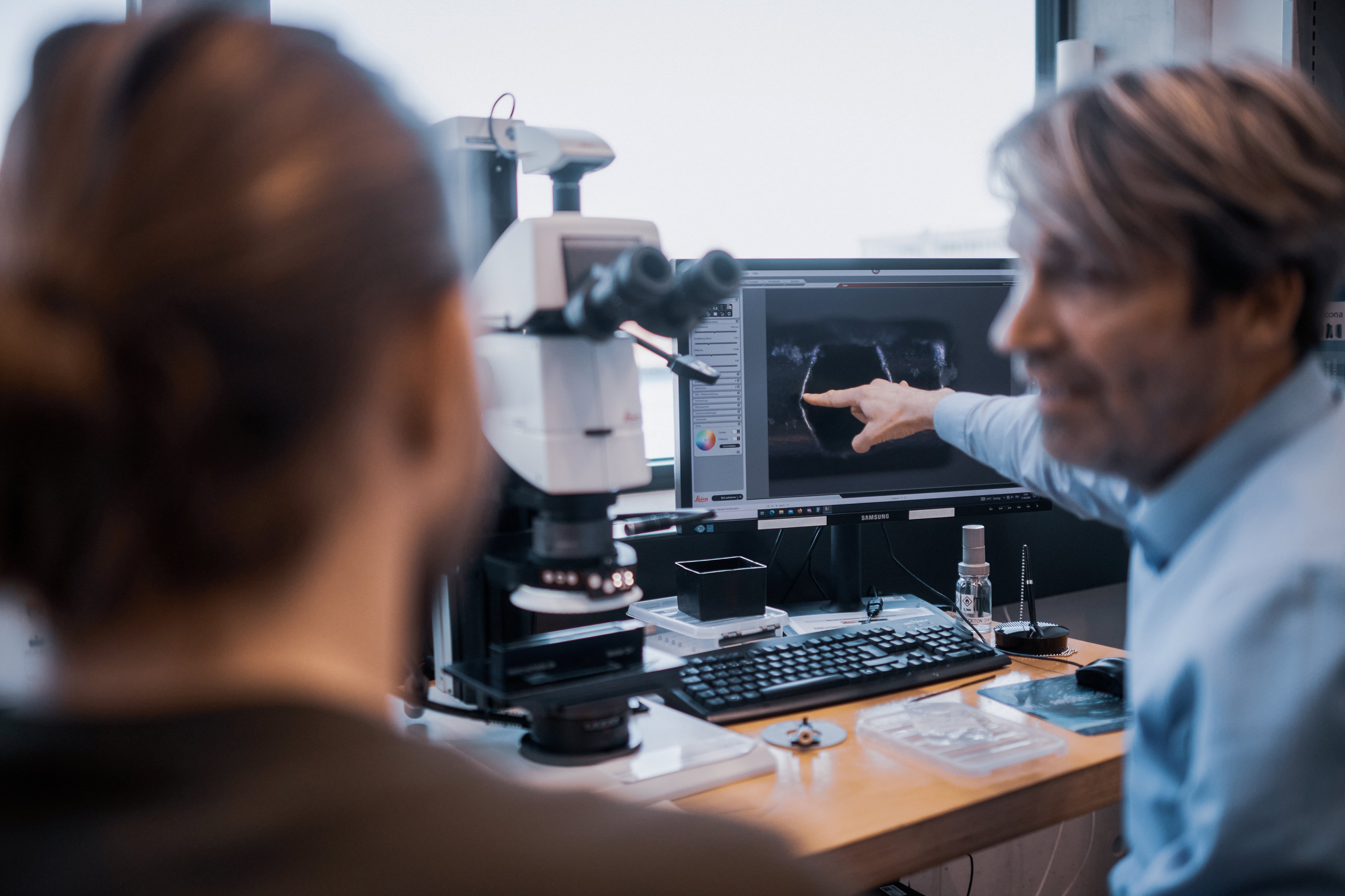 Mitarbeitende analysieren ophthalmologische Bildaufnahmen an einem Arbeitsplatz mit Mikroskop und Monitor in einer Büroumgebung