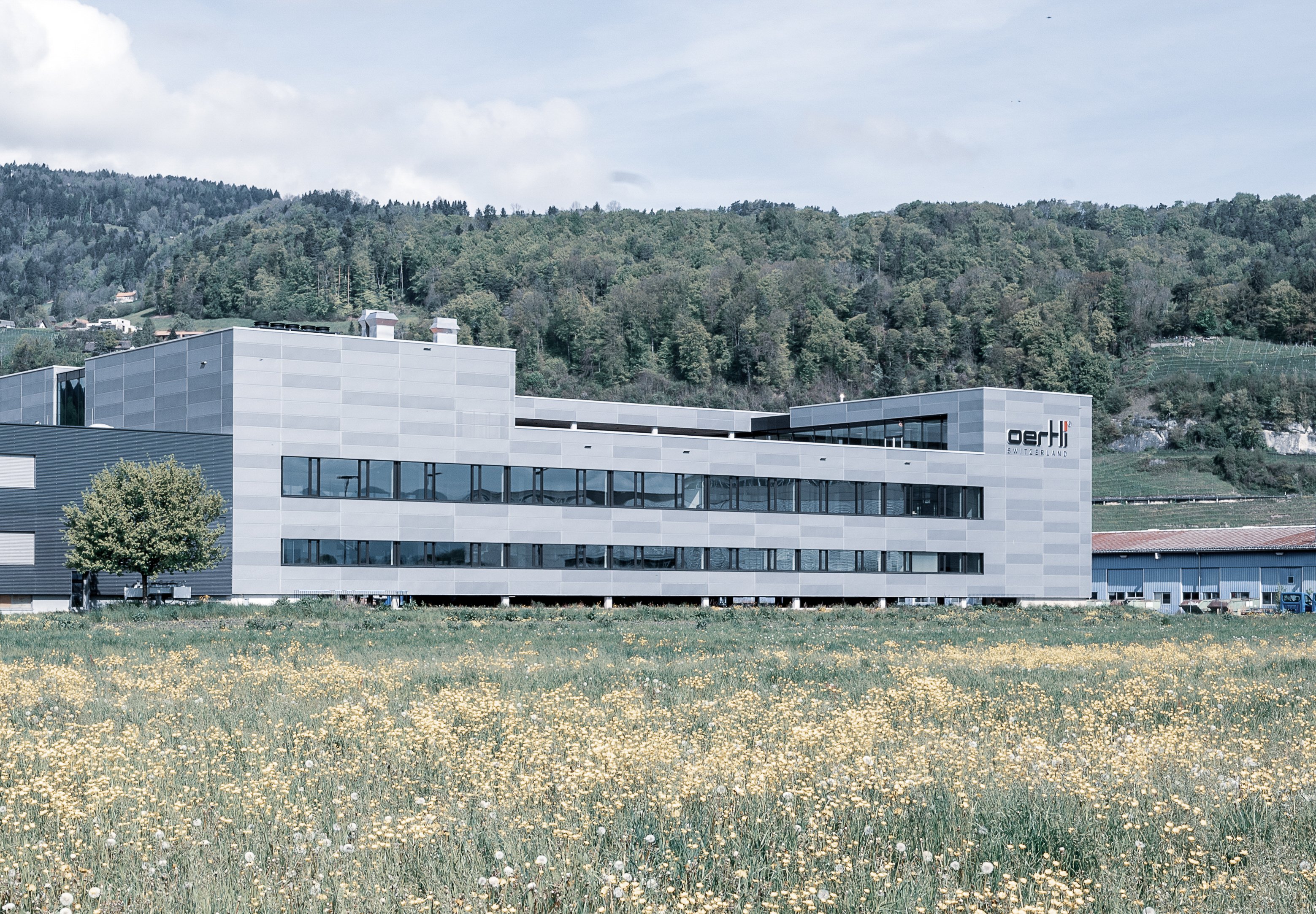 Oertli Lean Factory building surrounded by meadow and hillside landscape