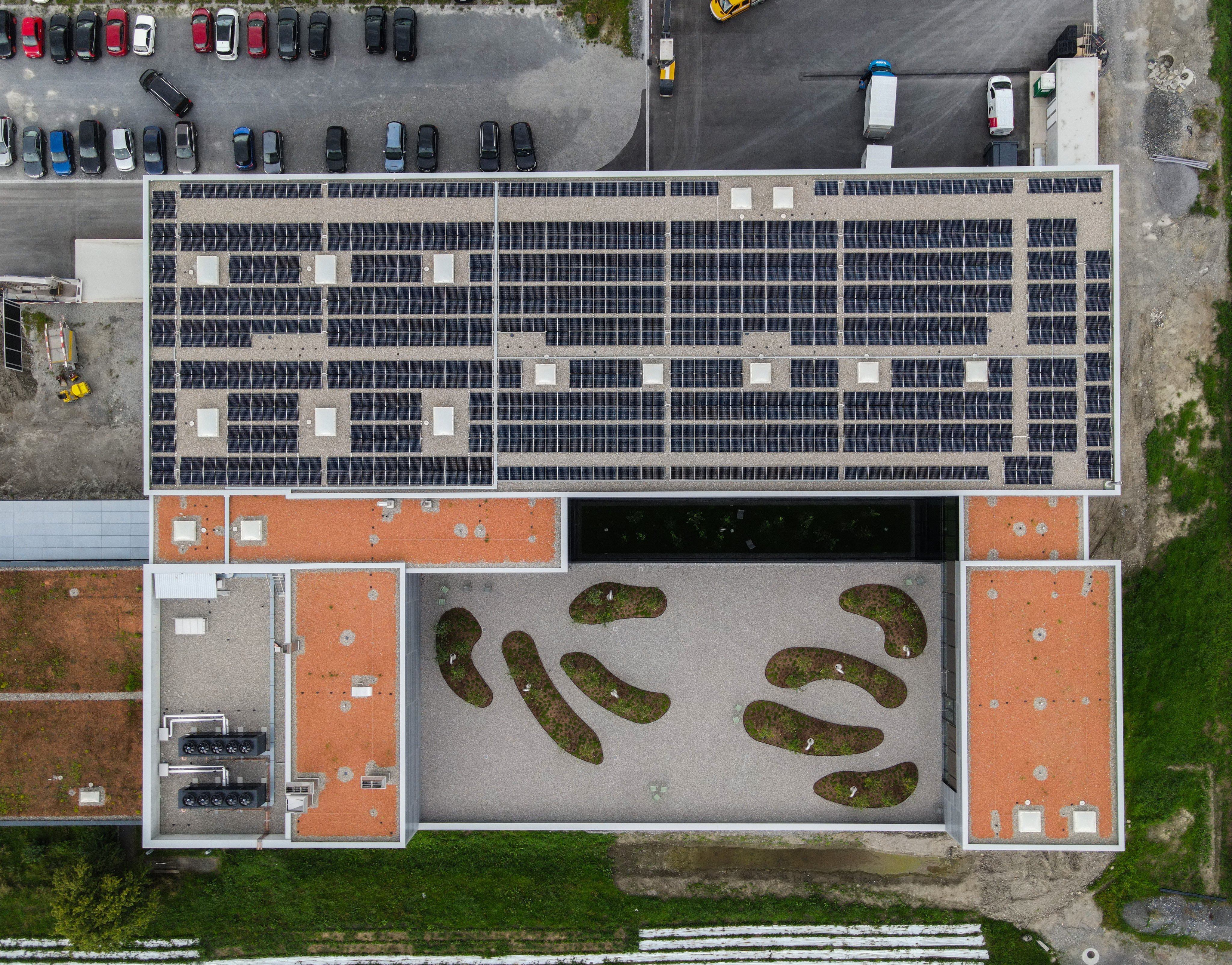 Drone view of the Oertli facility with photovoltaic panels installed across the rooftop. The building complex, landscaped courtyard and surrounding grounds are visible from above
