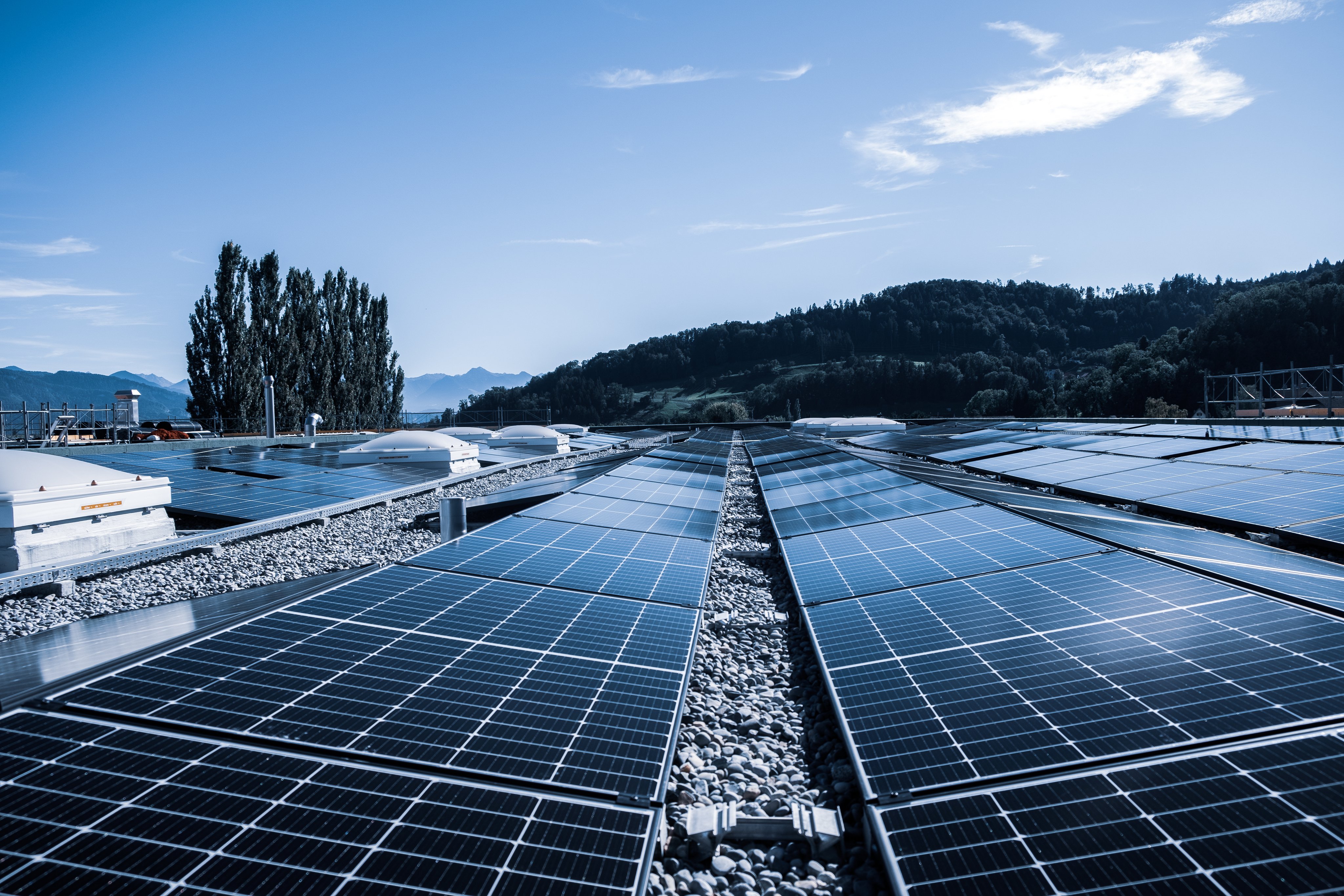 Solar panel installation on the rooftop of the Oertli building under a blue sky with hills and mountains in the background.