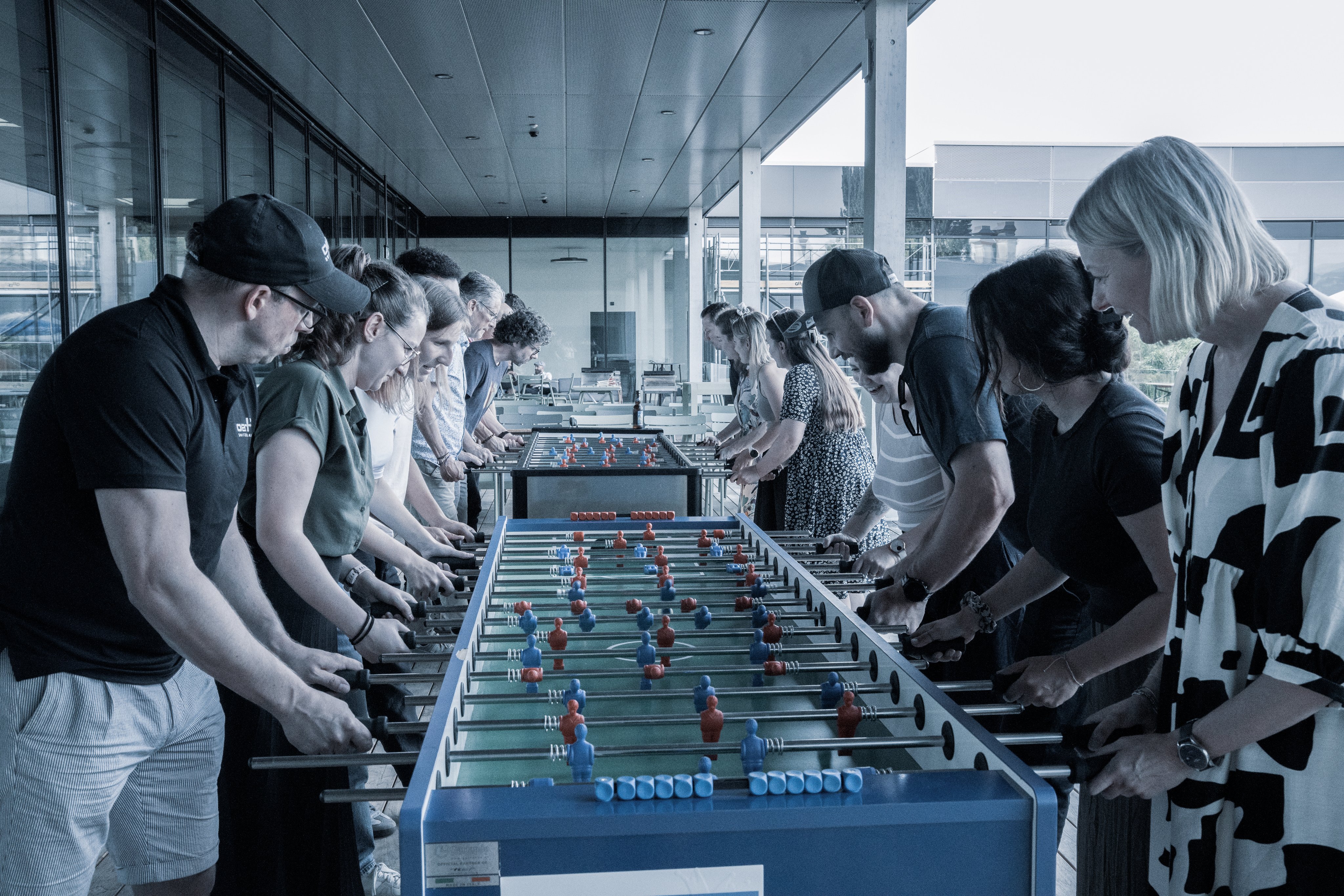 Mitarbeitende spielen gemeinsam Tischfussball in einem Aufenthaltsbereich im freien auf der Dachterasse