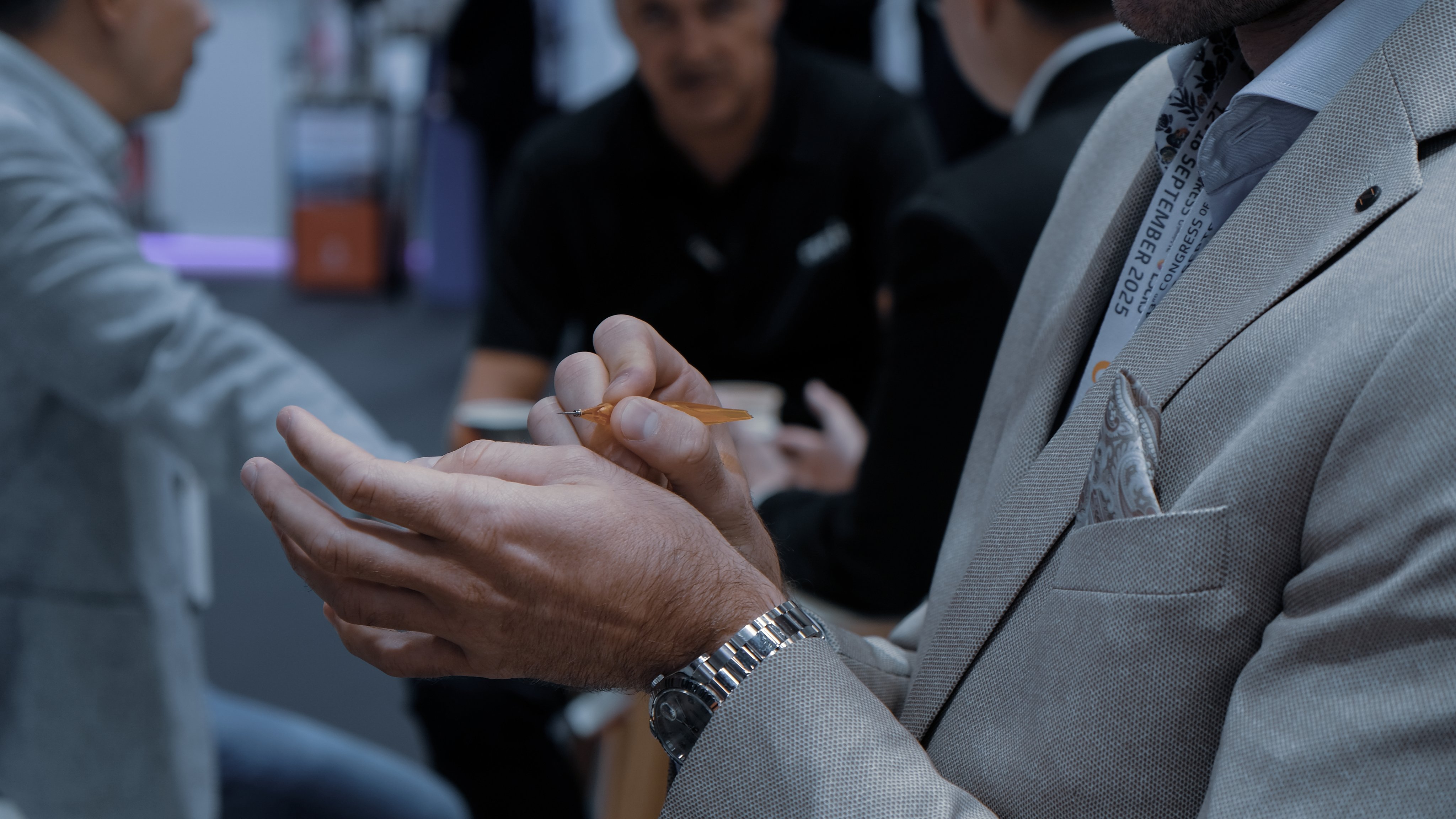 Close-up of a booth talk demonstration at ESCRS 2025, with a presenter holding a surgical instrument while attendees discuss in the background