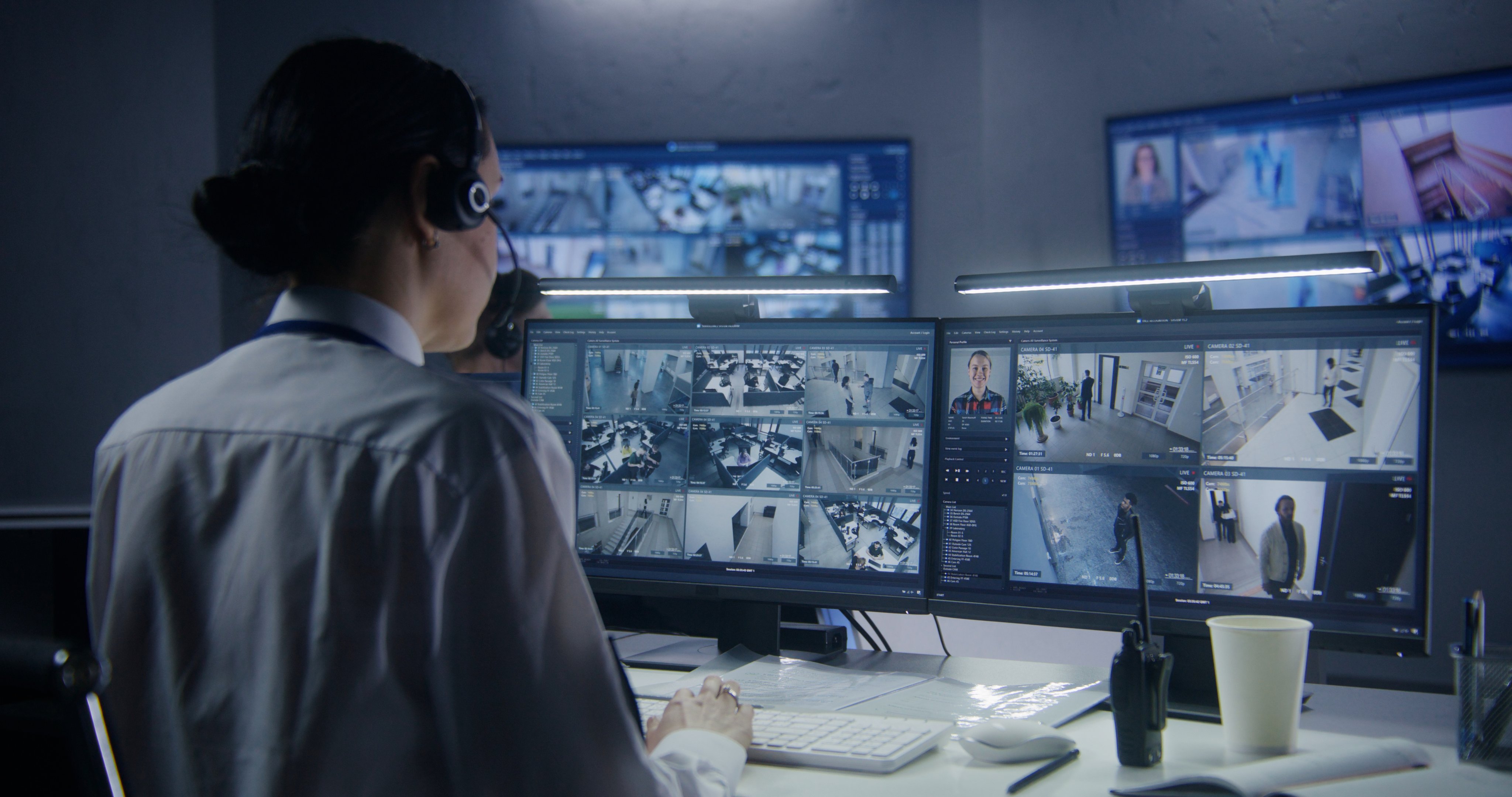 Female security officer watches security cameras with AI facial recognition with male colleagues. Monitoring center workers. Computer monitors and big digital screens with CCTV cameras video footage.