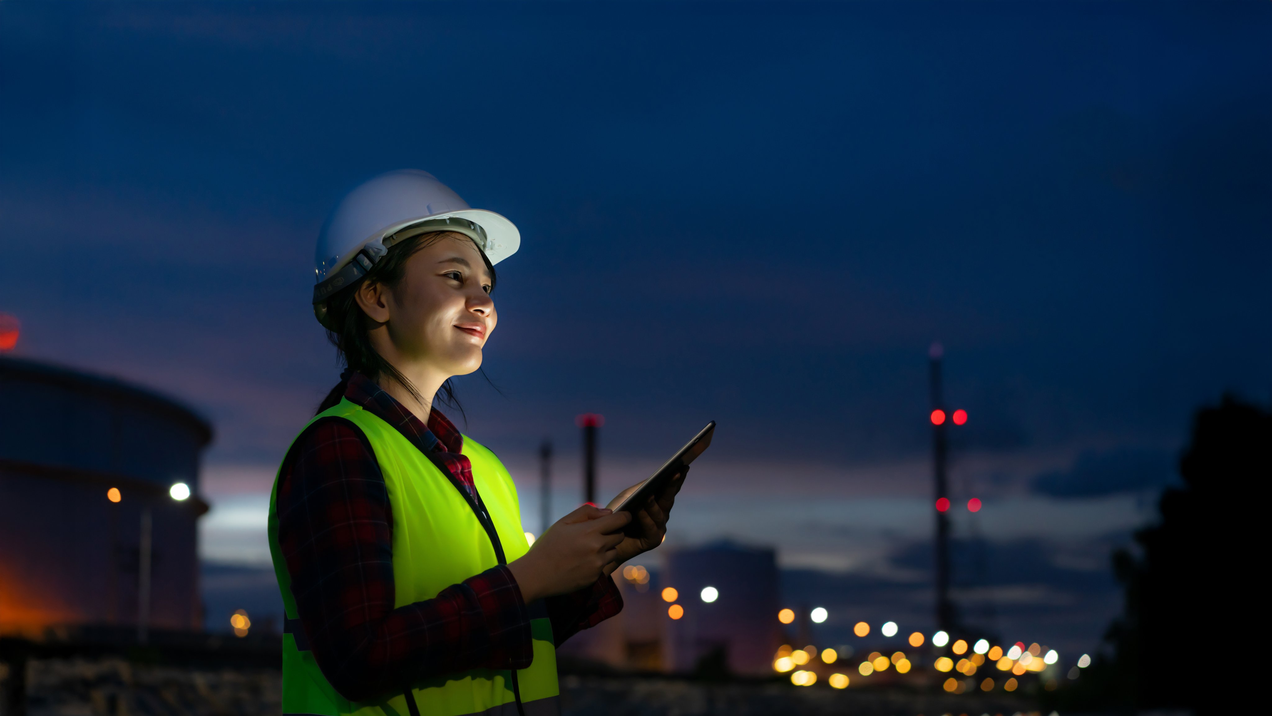 Asian woman petrochemical engineer working at night with digital tablet Inside oil and gas refinery plant industry factory at night for inspector safety quality control.
