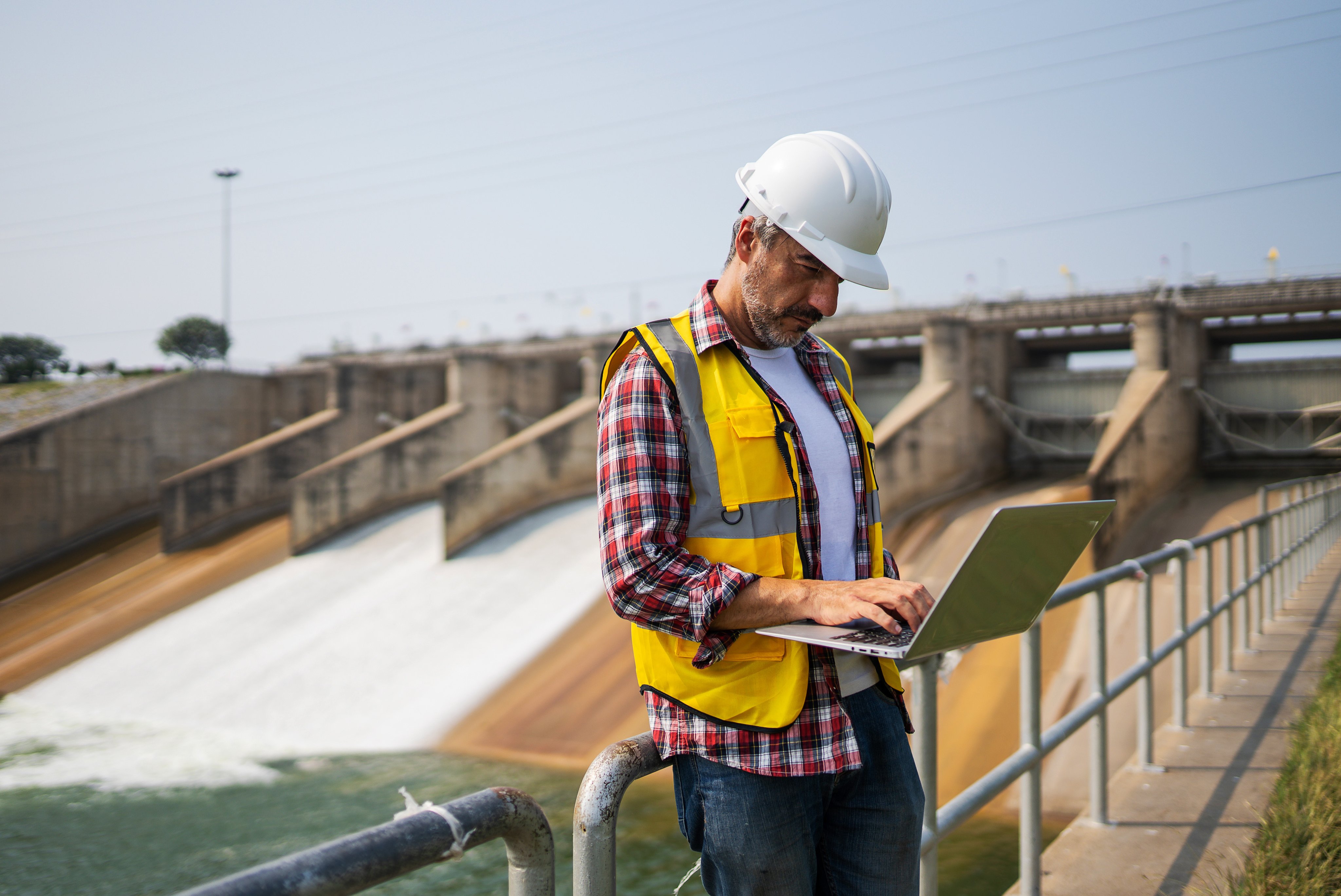 Portrait of engineer wearing yellow vest and white helmet with laptop computer Working day on a water dam with a hydroelectric power plant. Renewable energy systems, Sustainable energy concept