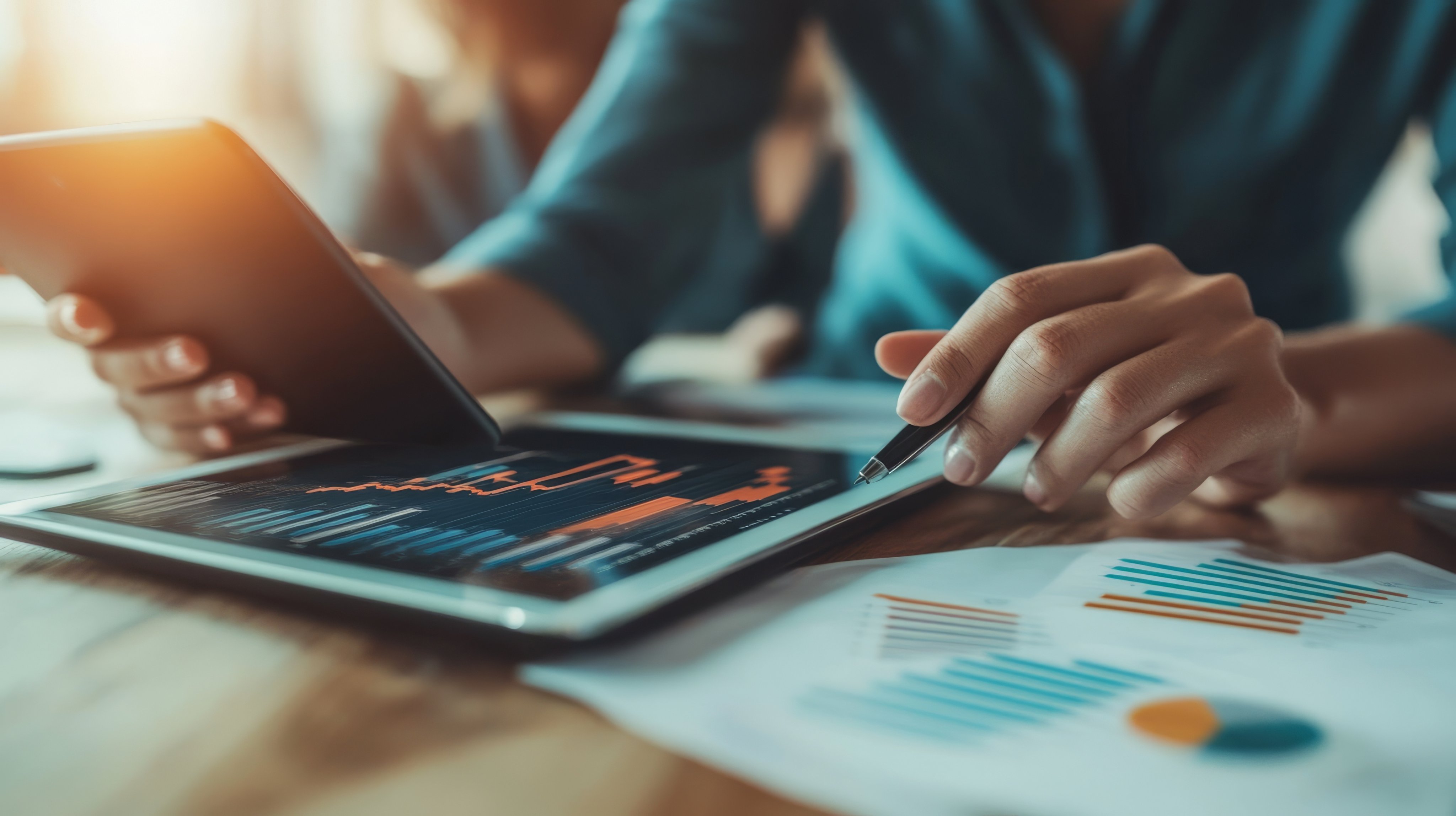 A person analyzes data on a tablet and smartphone, reviewing graphs and charts on papers, showcasing modern business and tech integration.