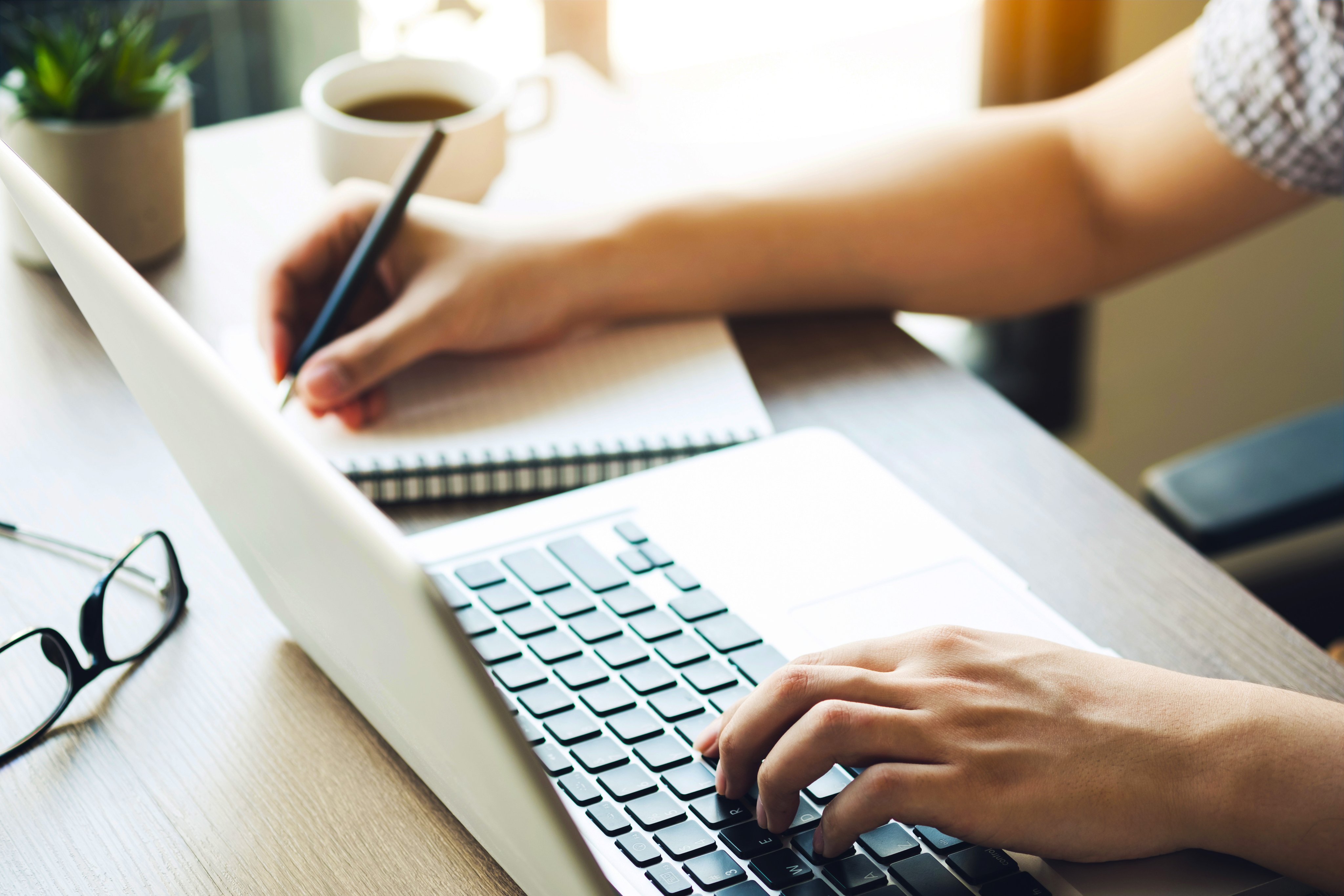 Young man is taking a note on a notebook from the internet research using laptop computer. Learning with technologies concept.