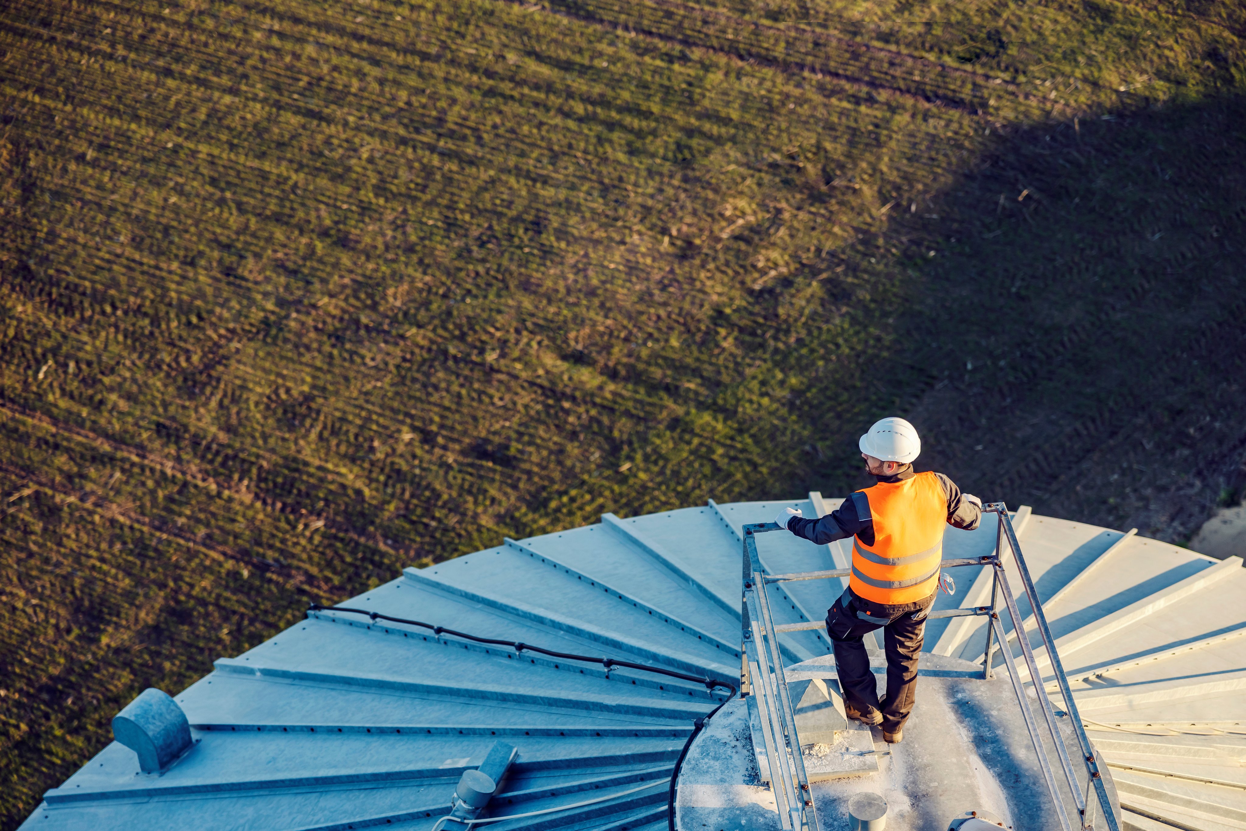 Aerial view of an industry worker leaning on railing on top of the silo and looking around.