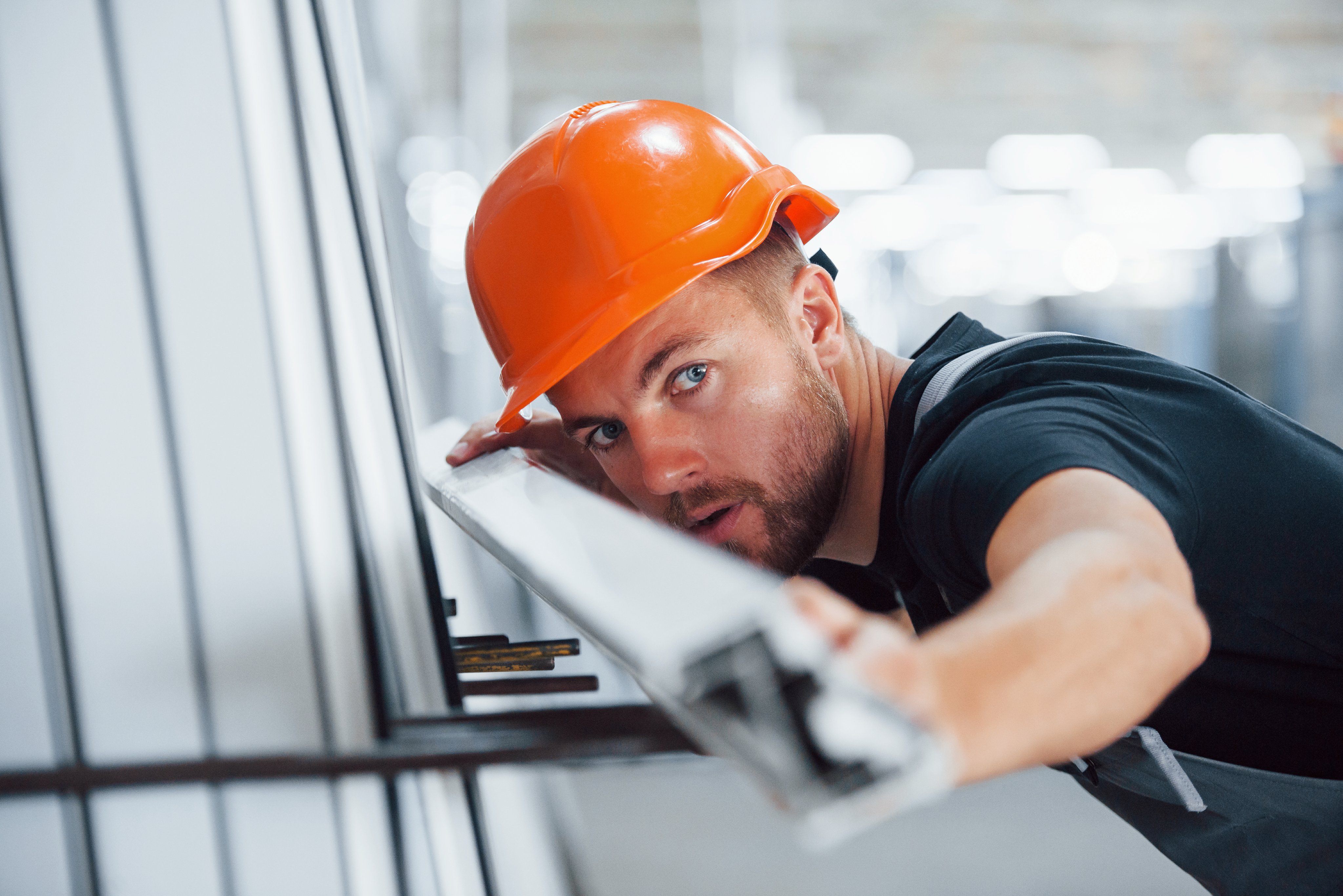 Measuring length of objects. Industrial worker indoors in factory. Young technician with orange hard hat.
