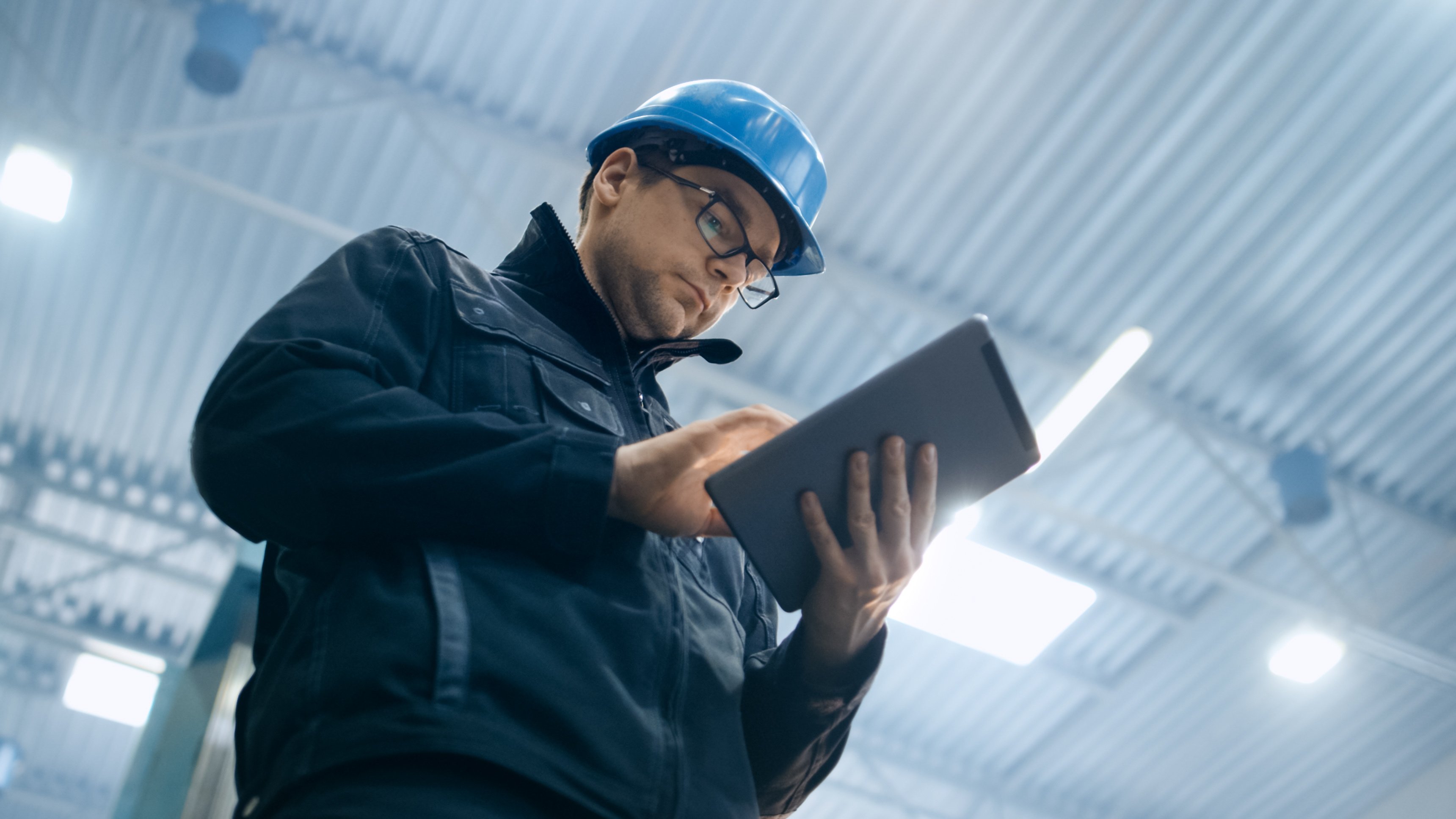 Factory worker in a hard hat is using a tablet computer.