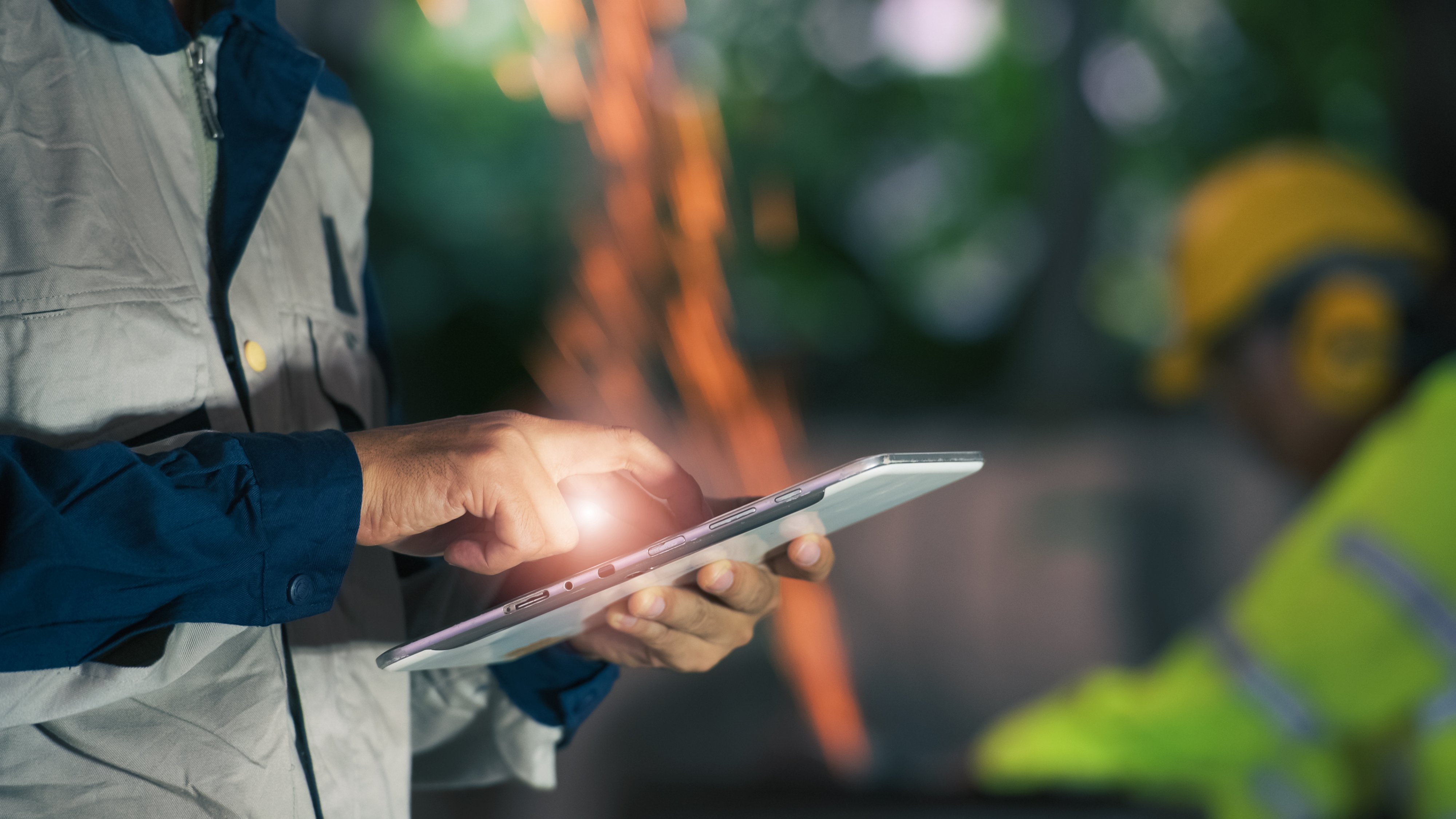 Asian workers, professional heavy industry engineers wearing safety suits and hard hats, use tablet computers. Asian industry professionals are in metallurgical plants.